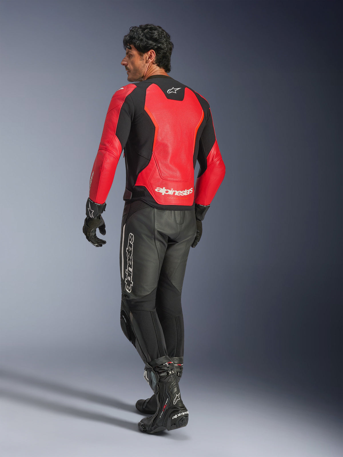 Alpinestars GP Force V2 Air Leather Jacket, Red and Black, rear view on a motorcycle rider, worn with black leather pants and racing boots, featuring perforated back panels and Alpinestars branding