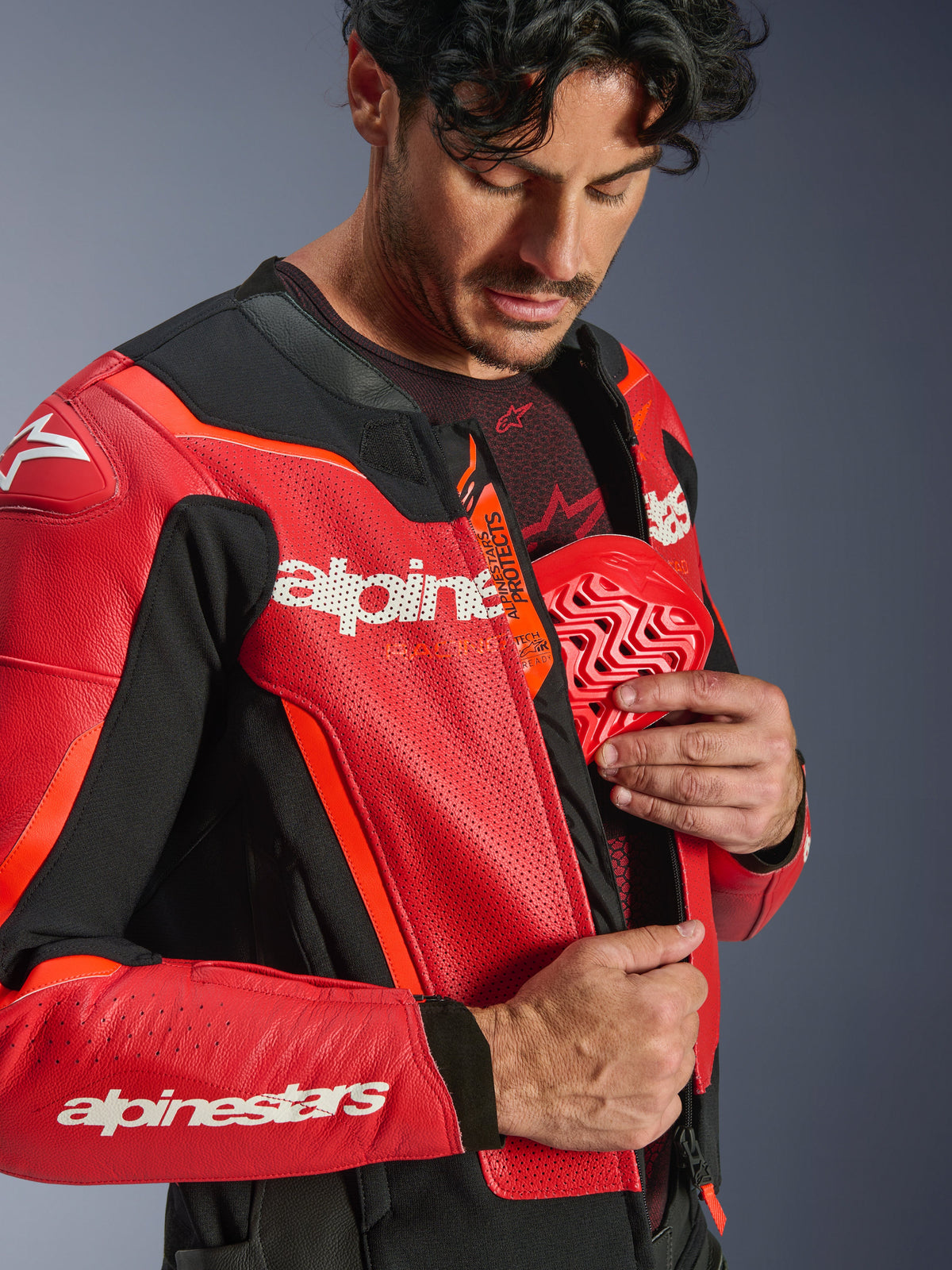 Alpinestars GP Force V2 Air Leather Jacket, Red and Red Fluo, close-up of a rider inserting a red chest protector into the inner pocket, featuring perforated leather and Tech-Air Ready logo, premium sport motorcycle protection.