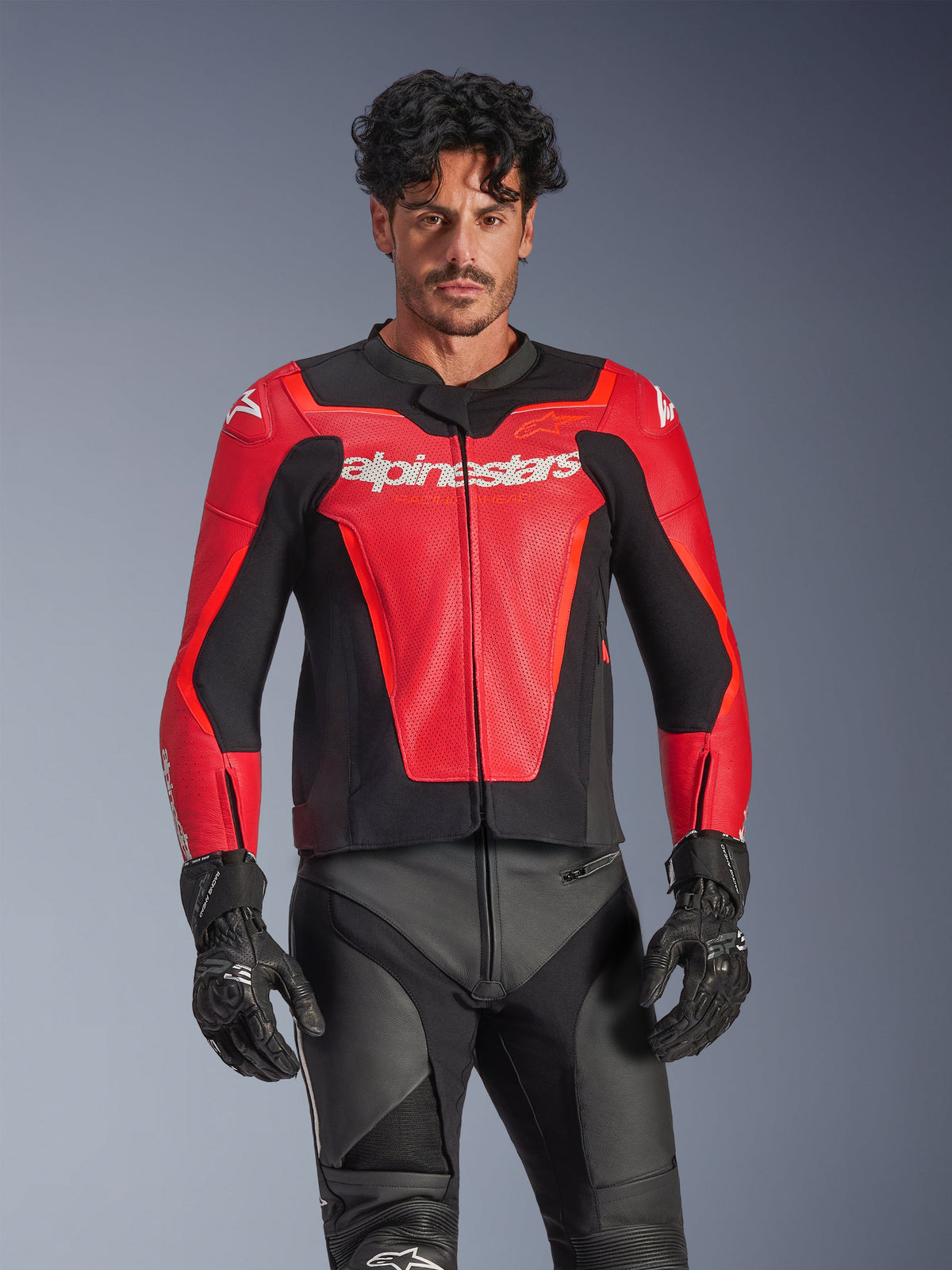 Alpinestars GP Force V2 Air Leather Jacket, Red and Black motorcycle racing jacket, perforated leather construction with white Alpinestars logo, worn by male model and paired with black racing pants and gloves