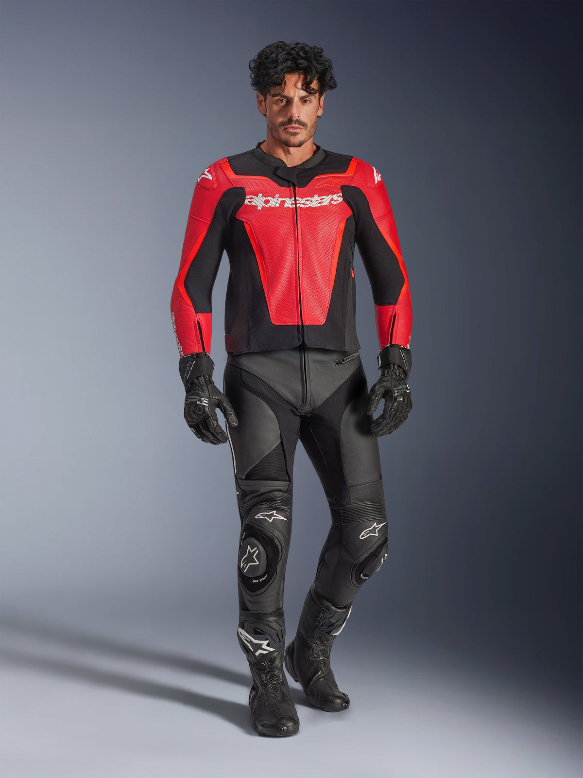 Alpinestars GP Force V2 Air Leather Jacket, Red and Black, perforated leather with white branding, worn by a model with black leather racing pants and gloves, professional motorcycle gear