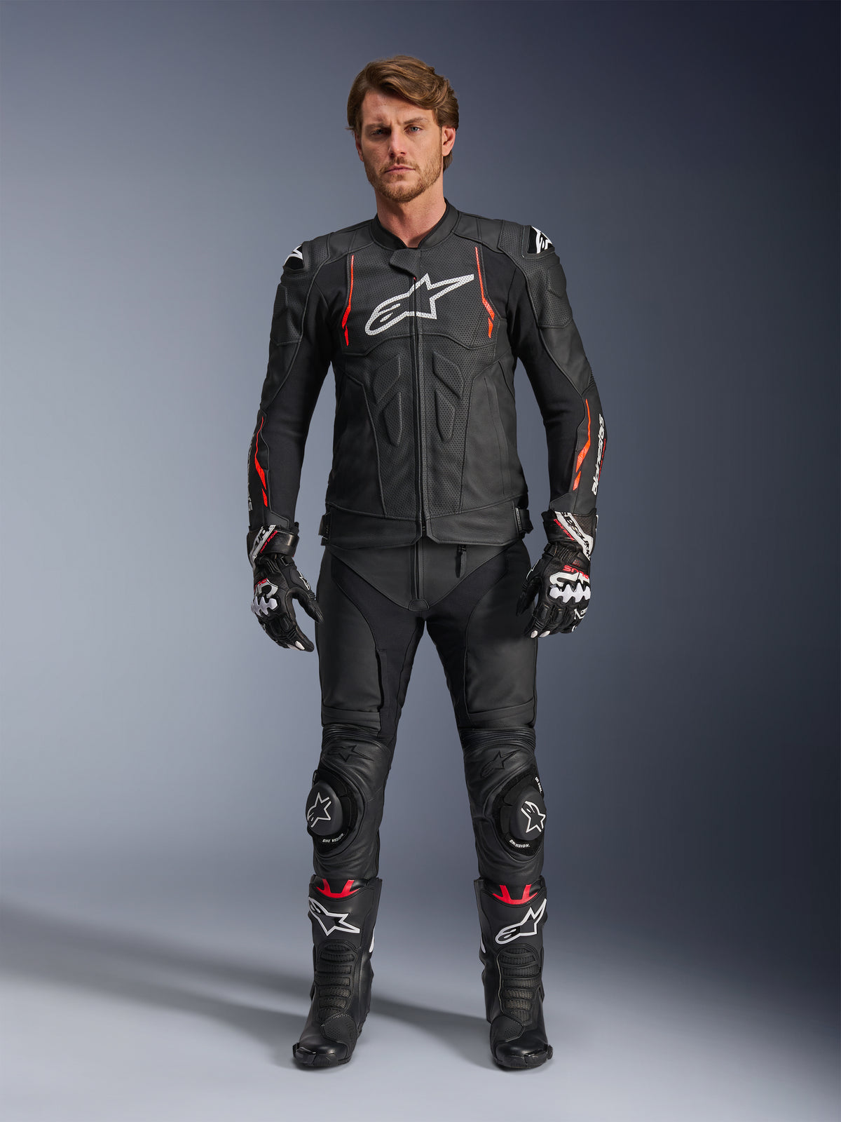 Male rider wearing the Alpinestars Dusk Airflow Leather Jacket in Black Red Fluo, featuring perforated leather panels and a white chest logo, paired with matching black leather riding pants, knee sliders, gloves, and racing boots, complete motorcycle road gear outfit.