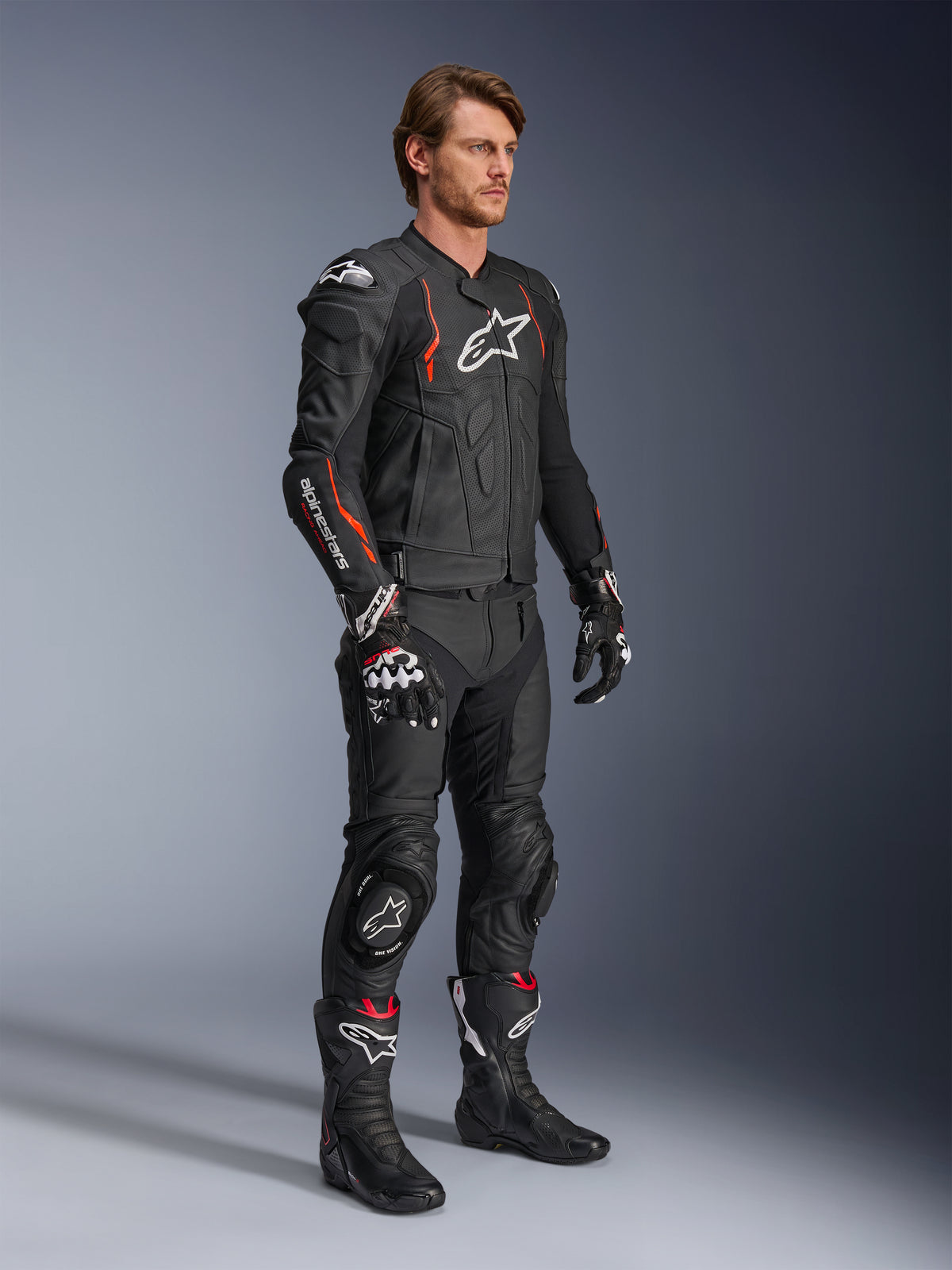 Alpinestars Dusk Airflow Leather Jacket, Black Red Fluo, worn as part of a complete motorcycle racing outfit with matching leather pants, gloves, and boots, featuring perforated leather construction and sporty accents.