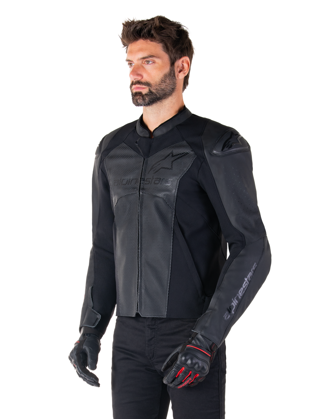 Modell trägt die Alpinestars Faster V3 Airflow Lederjacke in Schwarz, Sport-Motorradjacke mit perforiertem Leder und Stretch-Einsätzen, kombiniert mit schwarzer Hose und schwarzen Handschuhen mit roten Akzenten, eleganter, vom Rennsport inspirierter Stil.