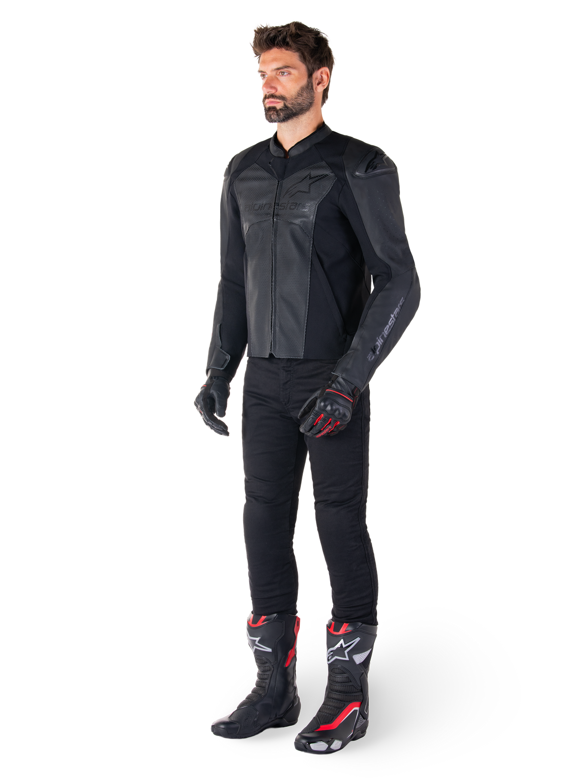 Mann in Alpinestars Faster V3 Airflow Lederjacke in Schwarz-Schwarz, kombiniert mit schwarzer Hose, schwarz-roten Motorradhandschuhen und schwarzen Rennstiefeln mit roten und weißen Akzenten, komplette Sport-Fahrerausrüstung