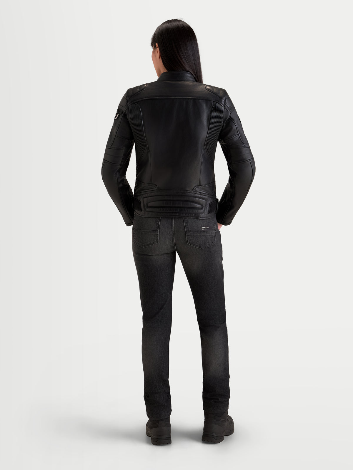 Alpinestars Revea Damen Lederjacke, urbane Damen-Motorradlederjacke in Schwarz, Rückansicht an einem Model mit dunklen Jeans und Motorradstiefeln, Vollnarbenrindleder-Konstruktion