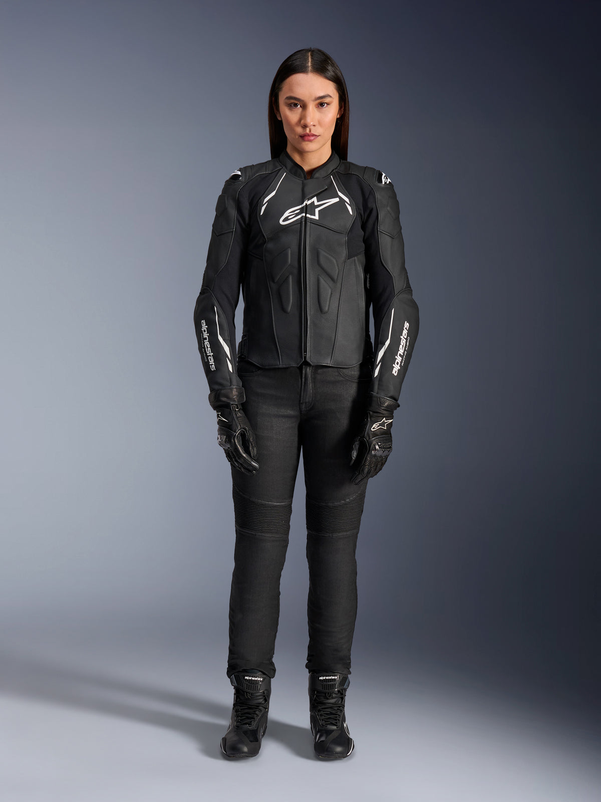 Alpinestars Woman Stella Dusk Leather Jacket, Black and White, worn by a model with matching black pants and boots, front view, featuring white Alpinestars logos on the chest and sleeves, premium bovine leather protective gear for women