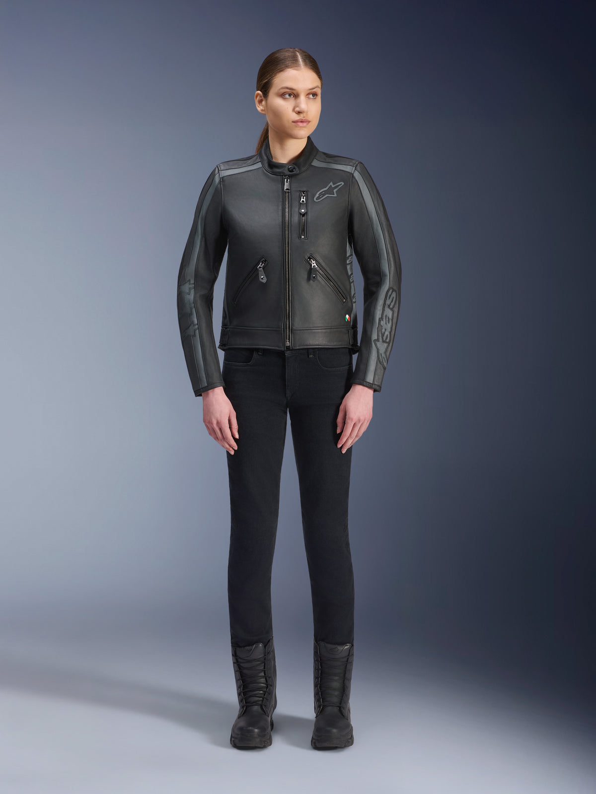 Alpinestars Stella Dyno Lederjacke, Damen-Motorradjacke, Schwarz, Tar Gray, Dunkelgrau, Ganzkörper-Studioansicht eines Models, das die Jacke mit einer schwarzen Slim-Fit-Hose und schwarzen Stiefeln trägt, gefertigt aus Rindsleder mit grauen Akzenten und dezentem Alpinestars-Branding auf der Brust und den Ärmeln.