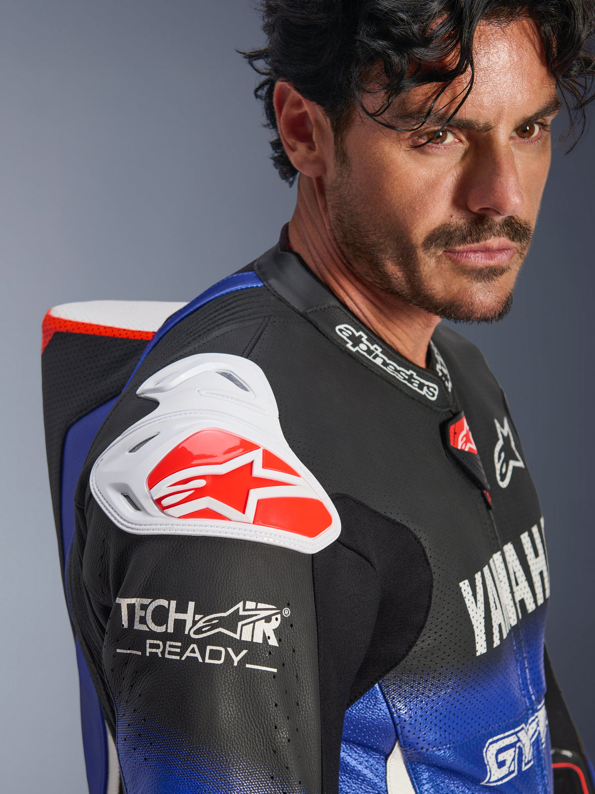 Yamaha GP-R7 Einteiliger Lederanzug, Metallic-Blau, Schwarz, Weiß und Rot, Nahaufnahme von Schulter und Brust, mit weißem DFS-Schulterschutz mit rotem Logo, aerodynamischem Höcker und Tech-Air Ready Branding auf dem perforierten Lederärmel.