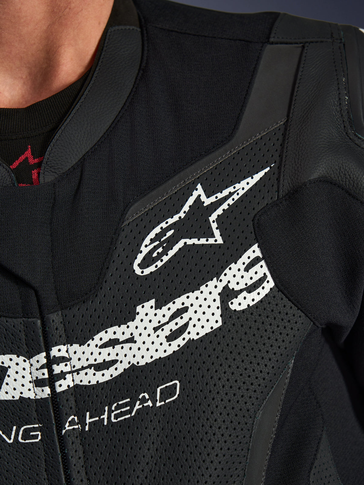 Alpinestars GP Force V2 Lederkombi 1-teilig, Nahaufnahme des Brustbereichs, schwarzes perforiertes Leder mit großem weißem Alpinestars-Logo, technische Sport-Fahrausrüstung, detaillierte Textur und Branding