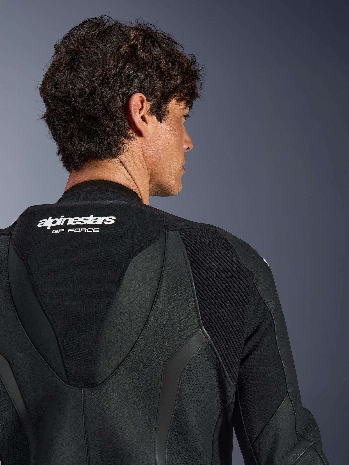 Alpinestars GP Force V2 Lederkombi 1-teilig, Schwarz, Nahaufnahme des oberen Rückens und des aerodynamischen Speed-Humps, mit weißem Branding, perforierten Lederbereichen und Akkordeon-Stretcheinsätzen für den Rennsport.