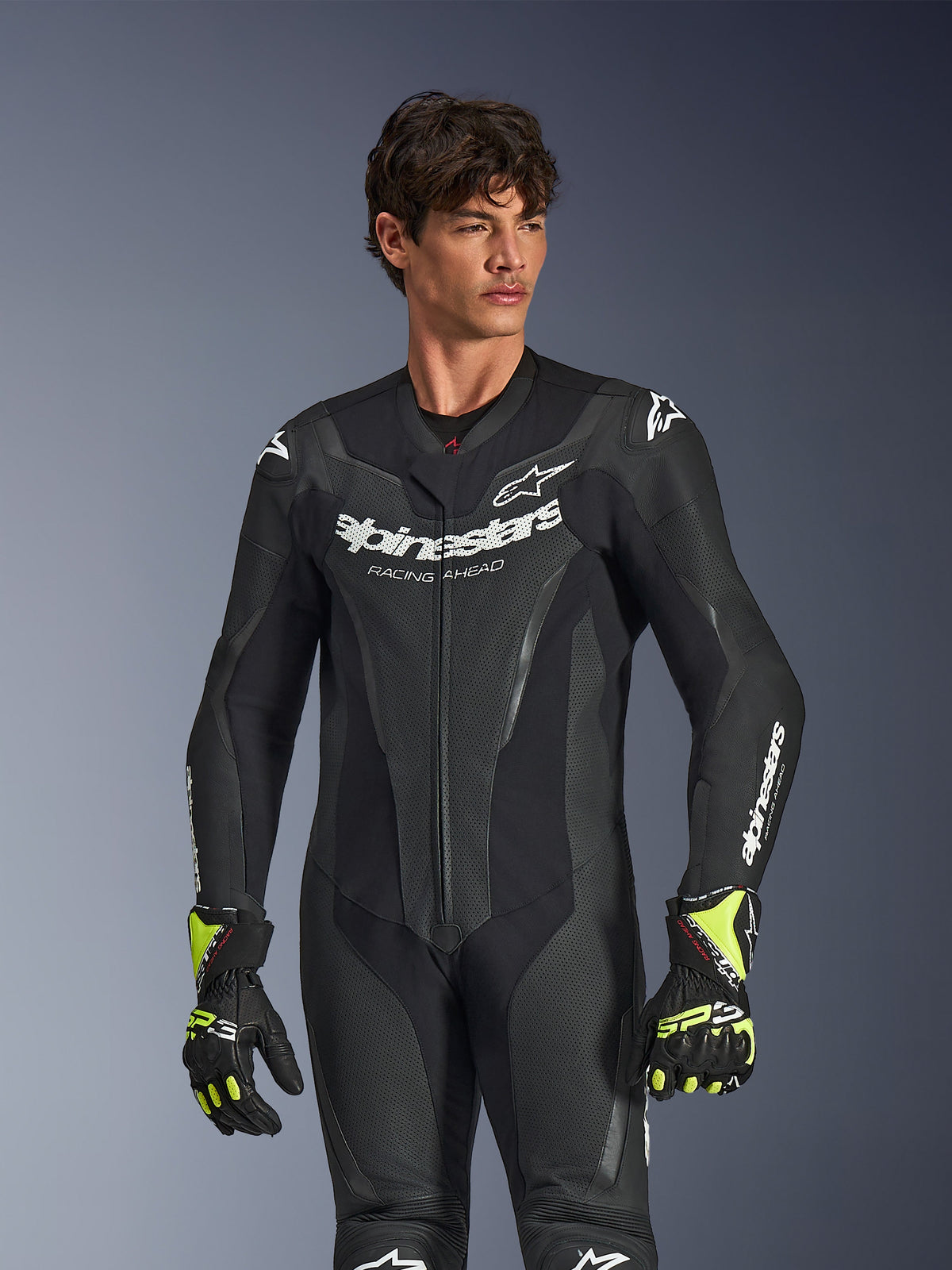 Alpinestars GP Force V2 Lederkombi 1-teilig, Schwarz, weißes Alpinestars-Branding und Logo, perforierte Lederpaneele zur Belüftung, getragen von einem männlichen Model mit schwarz-neon-gelben Handschuhen, Hochleistungs-Motorrad-Rennausrüstung