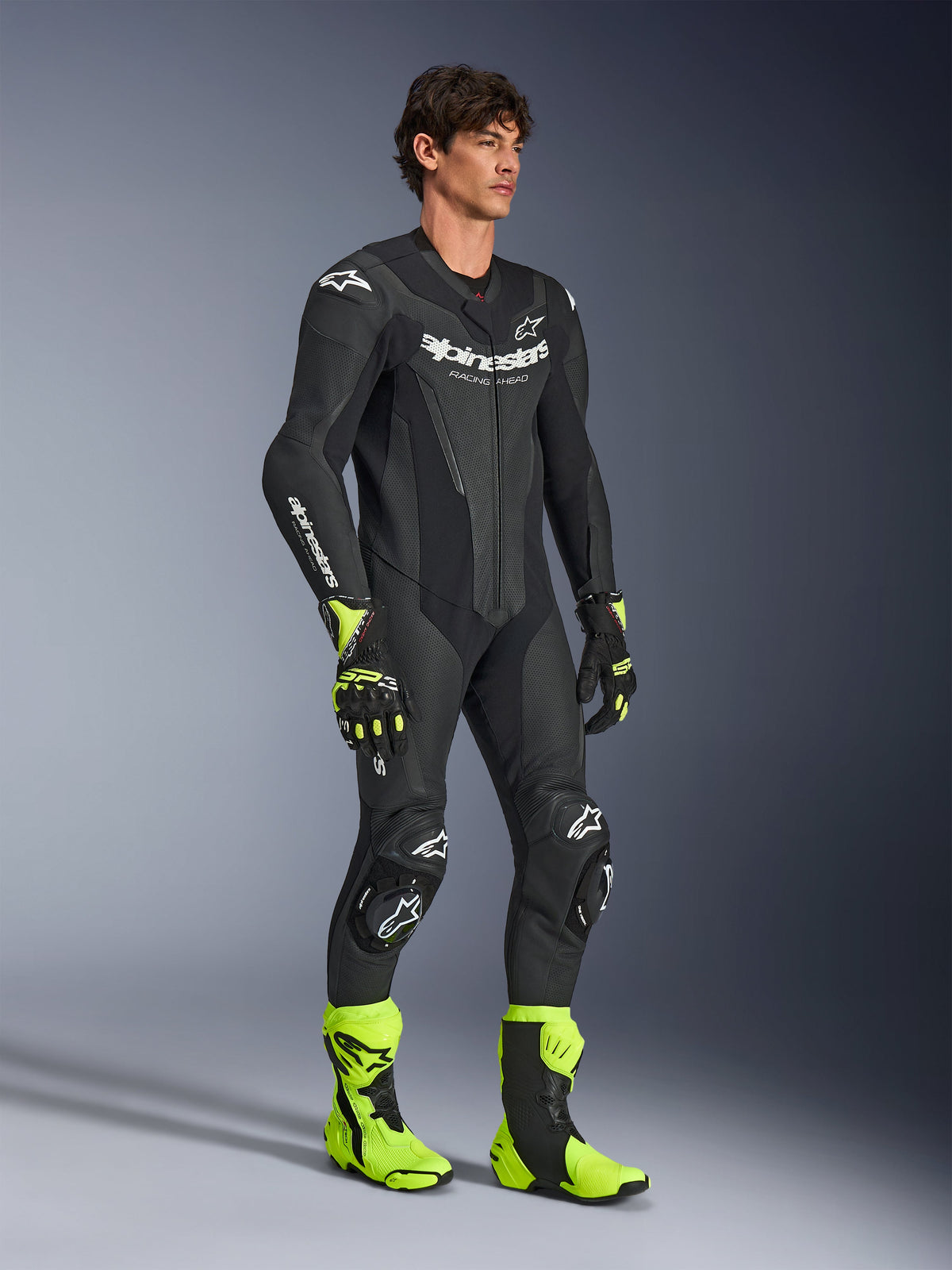 Mann präsentiert den Alpinestars GP Force V2 Lederkombi 1-Teiler in Schwarz, mit weißem Alpinestars-Branding, perforierten Lederbereichen und integrierten Protektoren, kombiniert mit neongelben und schwarzen Rennstiefeln und Handschuhen