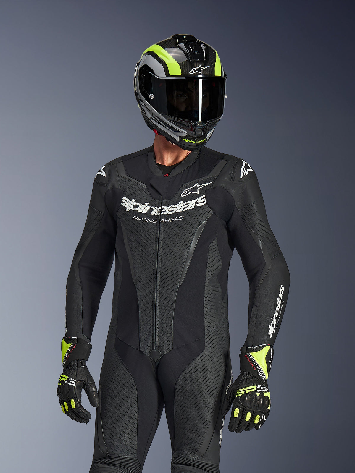 Alpinestars GP Force V2 Lederkombi 1-teilig, Schwarz, getragen von einem Fahrer mit einem schwarz-neongelben Helm und Handschuhen, mit weißem Alpinestars-Branding auf der Brust, perforierten Lederpaneelen zur Belüftung und einem professionellen, rennbereiten Design.