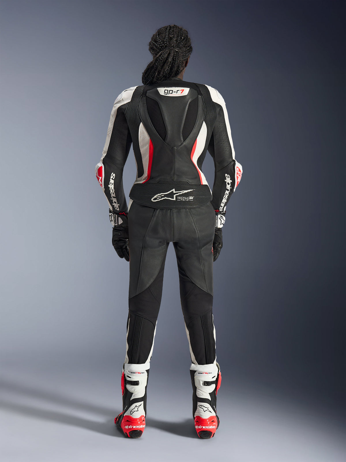Rückansicht des Alpinestars Stella GP-R7 2-teiligen Lederanzugs, Schwarz, Weiß und Fluo-Rot, mit einem aerodynamischen Höcker samt GP-R7-Branding und Tech-Air Ready-Logo, getragen mit passenden Rennstiefeln und Handschuhen, professionelle Motorradausrüstung für Damen