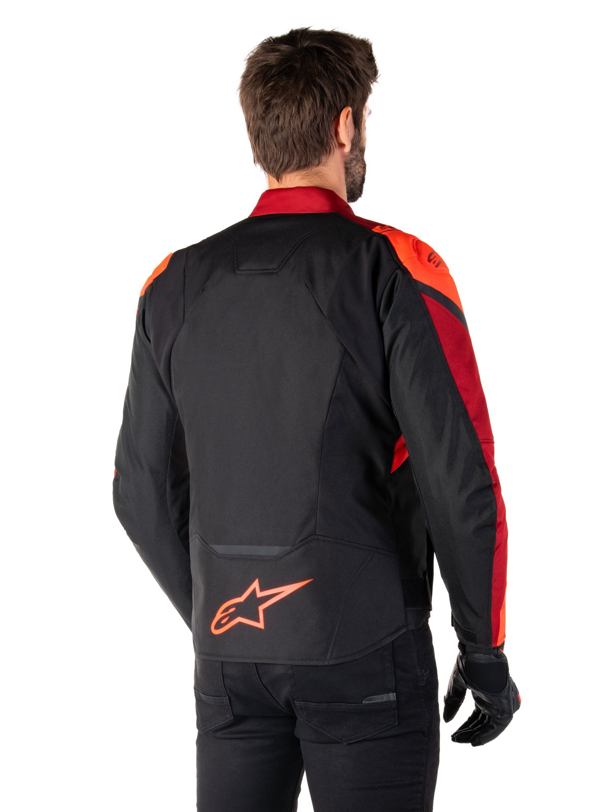 Rear view of a man wearing the Alpinestars T-Jaws V4 Waterproof Jacket in Black Red Fluo Dark Red, featuring vibrant red accents on the shoulders and sleeves, a fluo red Alpinestars logo on the lower back, paired with black pants and gloves.