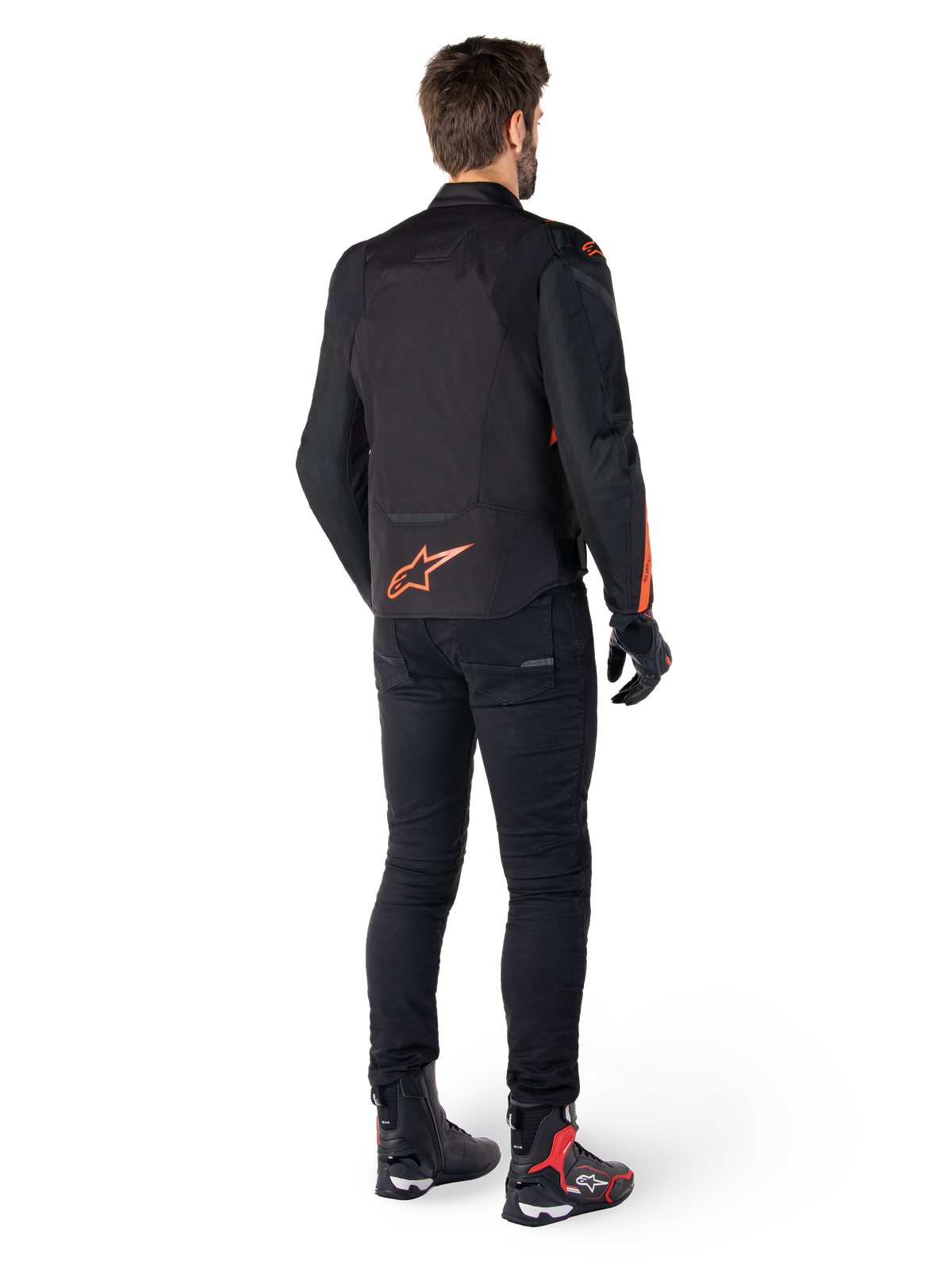 Alpinestars T-Jaws V4 Wasserdichte Jacke, Schwarz und Fluo-Rot, Rückansicht getragen von einem männlichen Fahrer, mit einem leuchtend roten Fluo-Logo auf dem Rücken, kombiniert mit schwarzer Motorradhose und technischen Stiefeln, sportliche Motorradbekleidung.
