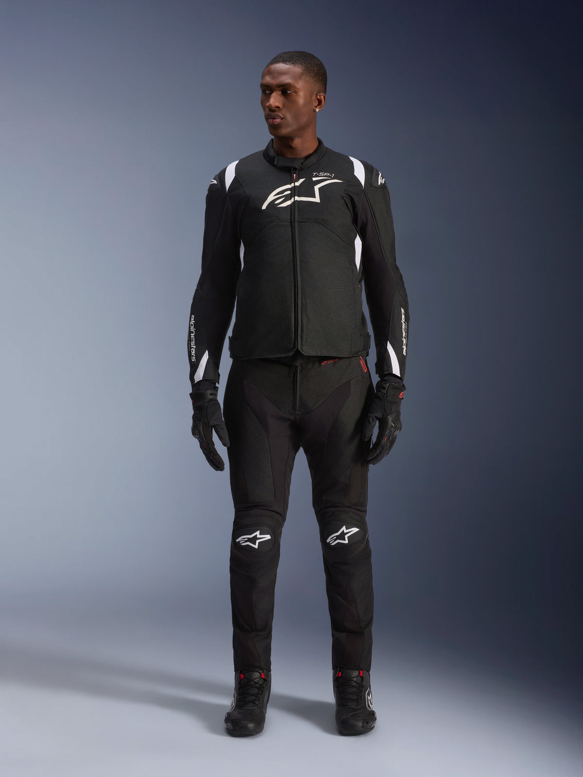 Alpinestars T-SP 1 V2 Waterproof Jacket, Black and White, featuring a prominent white chest logo and shoulder accents, worn with matching black motorcycle pants and gloves for a complete road riding look
