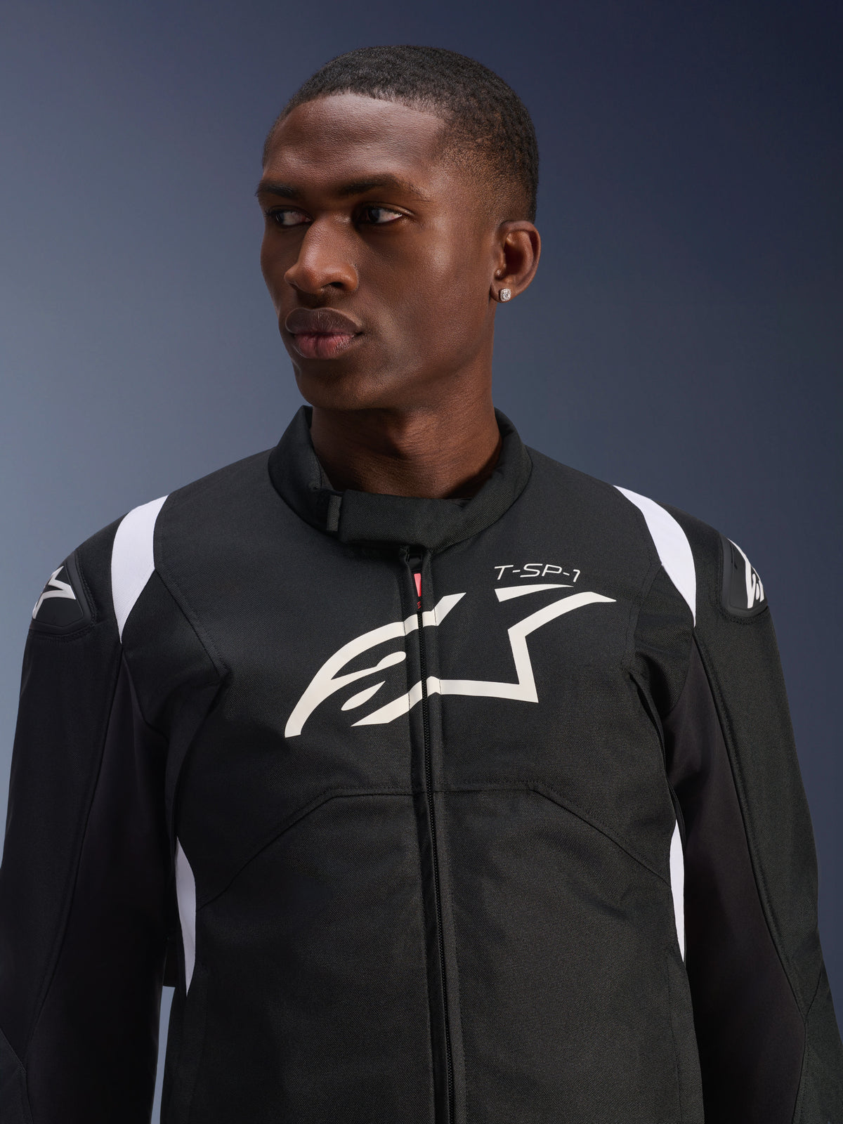 Alpinestars T-SP 1 V2 Waterproof Jacket worn by a model, black and white textile motorcycle jacket, large white Alpinestars logo and T-SP-1 branding on the chest, sporty design with protective shoulder sliders