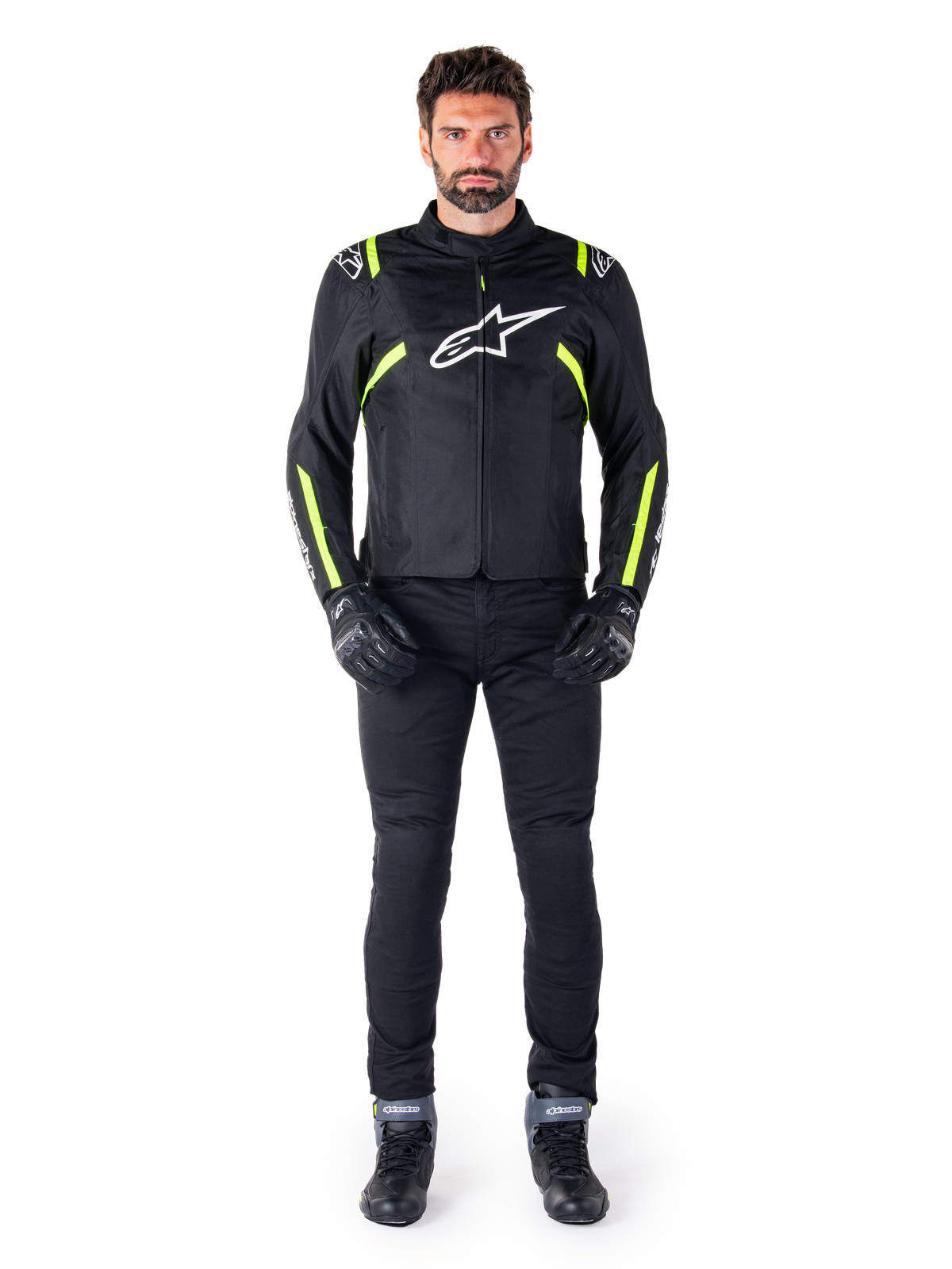 Alpinestars T-SPS V2 Waterproof Jacke, Schwarz, Weiß und Gelb Fluo, getragen von einem Model mit schwarzer Motorradhose und Handschuhen, mit weißem Alpinestars-Logo auf der Brust und fluoreszierenden Akzenten an Schultern und Ärmeln, sportlich geschnittene Motorradbekleidung