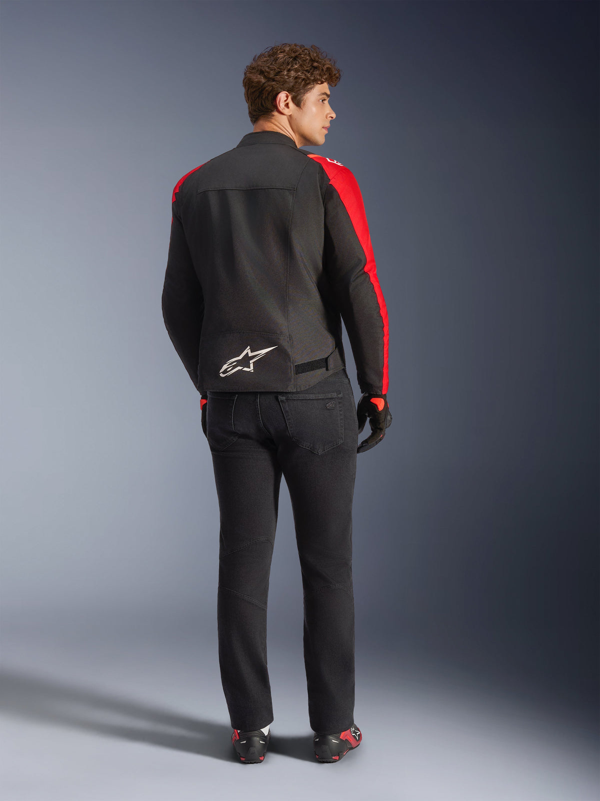 Alpinestars T-SPS V2 Waterproof Jacket, Black Red Red Fluo, back view on male model, white Alpinestars logo on the lower back, worn with black motorcycle pants and gloves, sporty textile waterproof riding jacket