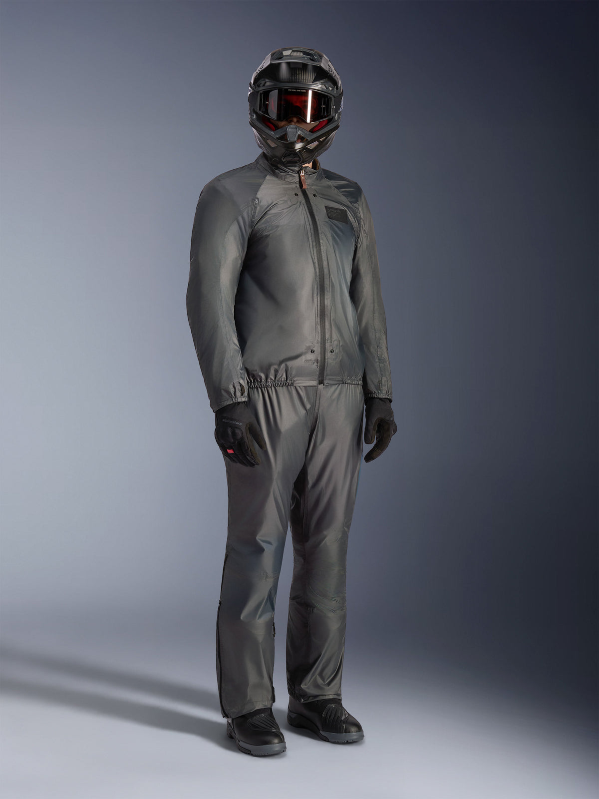 Fahrer trägt die Alpinestars Borrego Drystar® Jacke in Warm Gray, komplette Adventure-Ausrüstung mit passender grauer Hose, schwarzem Integralhelm mit Schutzbrille und schwarzen Handschuhen, im schlanken, wasserdichten Textildesign.