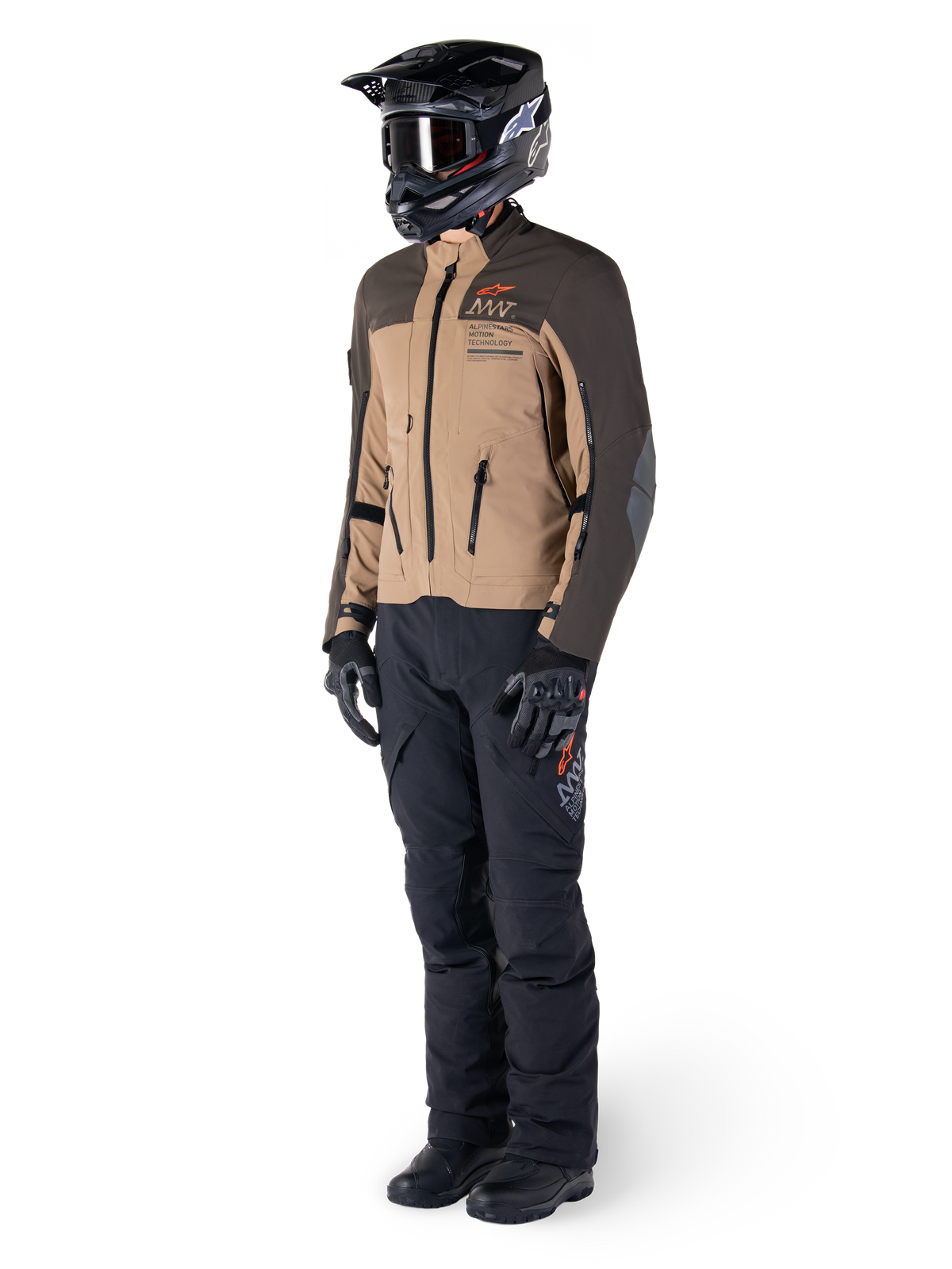 Adventure-Fahrer in kompletter Ausrüstung, Alpinestars AMT-8 Stretch Drystar® XF Jacke in Dunkelbraun und Dunkelkhaki, kombiniert mit schwarzer Adventure-Hose, schwarzem Helm, Handschuhen und Stiefeln, mit orangefarbenem AMT-Branding und technischen Belüftungsreißverschlüssen für Langstreckentouren
