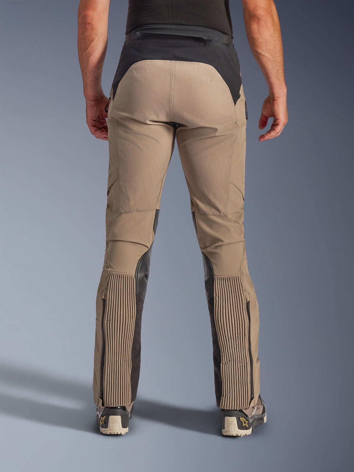 Alpinestars AMT-8 Stretch Drystar® XF Hose, Walnut Black, Rückansicht am Modell, hellbraunes Stretch-Textil-Hauptmaterial mit schwarzer Taillenpasse und Wadenbahnen, große Akkordeon-Stretcheinsätze an den Unterschenkeln, Beinabschlüsse mit Reißverschluss, Adventure-Touring-Passform.