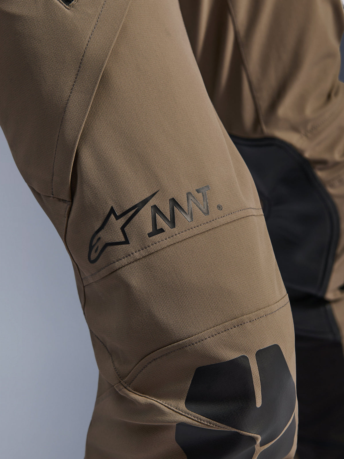Alpinestars AMT-8 Stretch Drystar® XF Hose in Walnut Black, Nahaufnahme des Beins mit dem schwarzen AMT-Logo und Alpinestars-Stern, leistungsstarkes Stretch-Gewebe mit schwarzen Einsätzen, technische Adventure-Motorradausrüstung