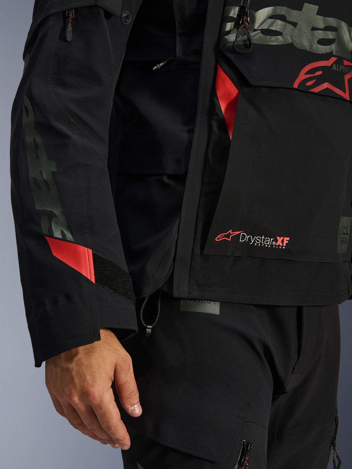 Alpinestars Halo Pro Drystar® XF Laminierte Jacke, Motorradjacke, Schwarz mit roten Akzenten, Nahaufnahme mit Drystar® XF Branding, technischer laminierter Materialstruktur und verstellbaren Ärmeldetails für Adventure-Fahrten