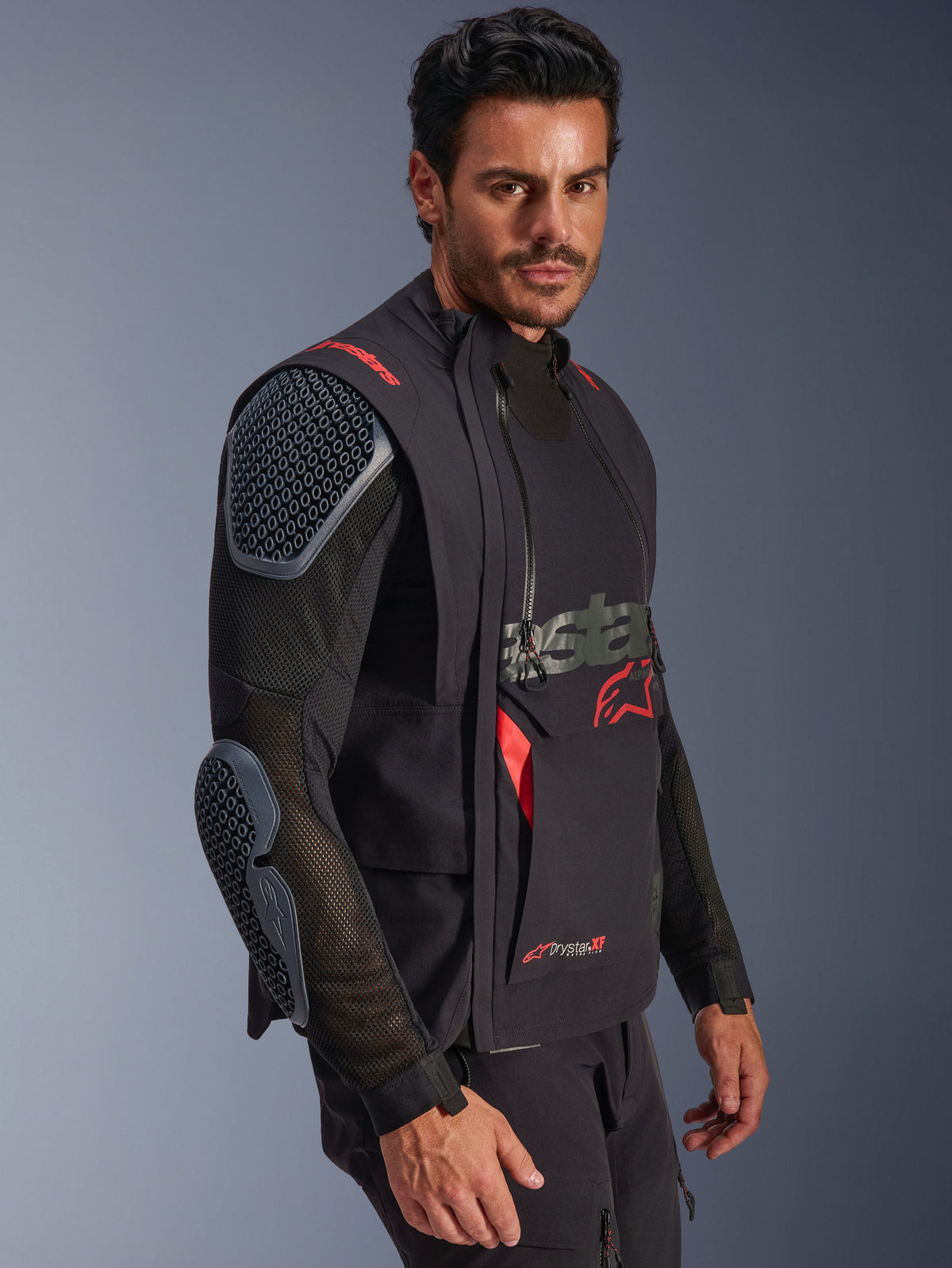 Alpinestars Halo Pro Drystar® XF Laminierte Jacke, Schwarz und Dark Shadow, Adventure-Motorradjacke am Modell, modulare Konfiguration mit Mesh-Ärmeln und integrierten Schulter- und Ellbogenprotektoren, rote Logo-Akzente und technische wasserdichte Reißverschlüsse.