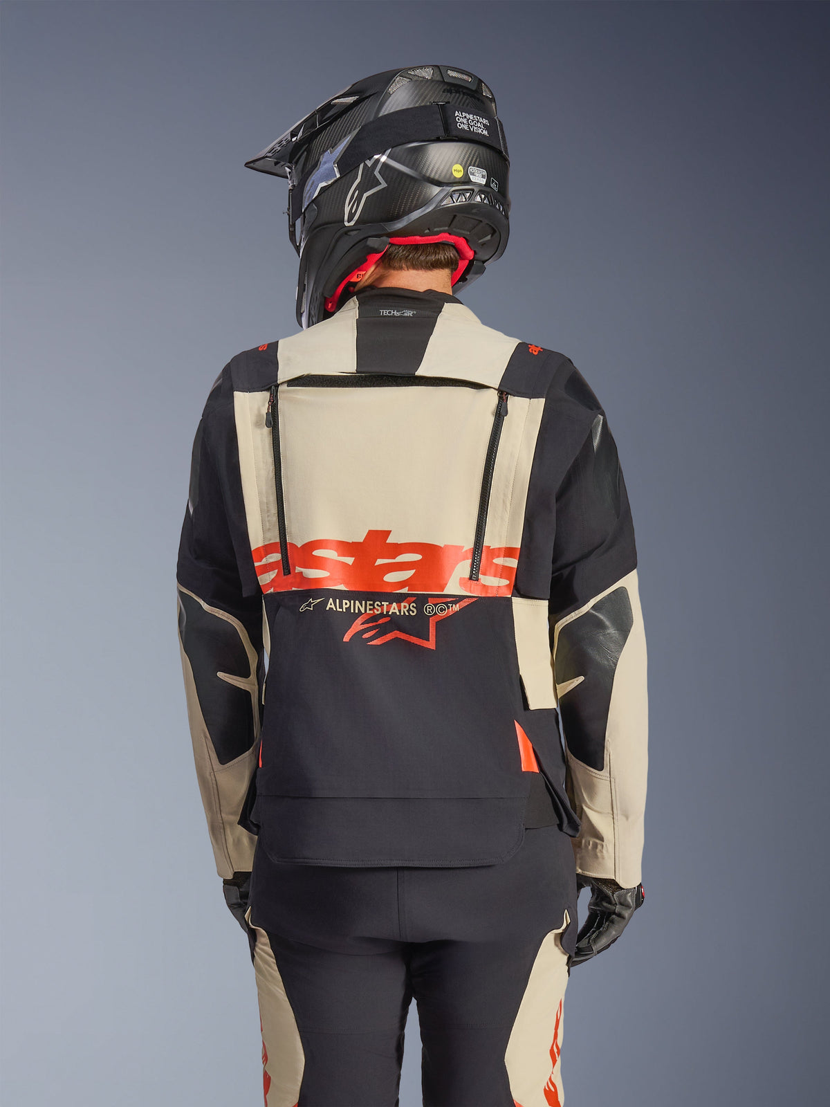 Alpinestars Halo Pro Drystar® XF Laminierte Jacke in Mastic Black, Rückansicht mit modularem Rückenpanel, rotem Logo und Belüftungsreißverschlüssen, getragen von einem Fahrer mit passender Adventure-Hose und einem schwarzen Helm