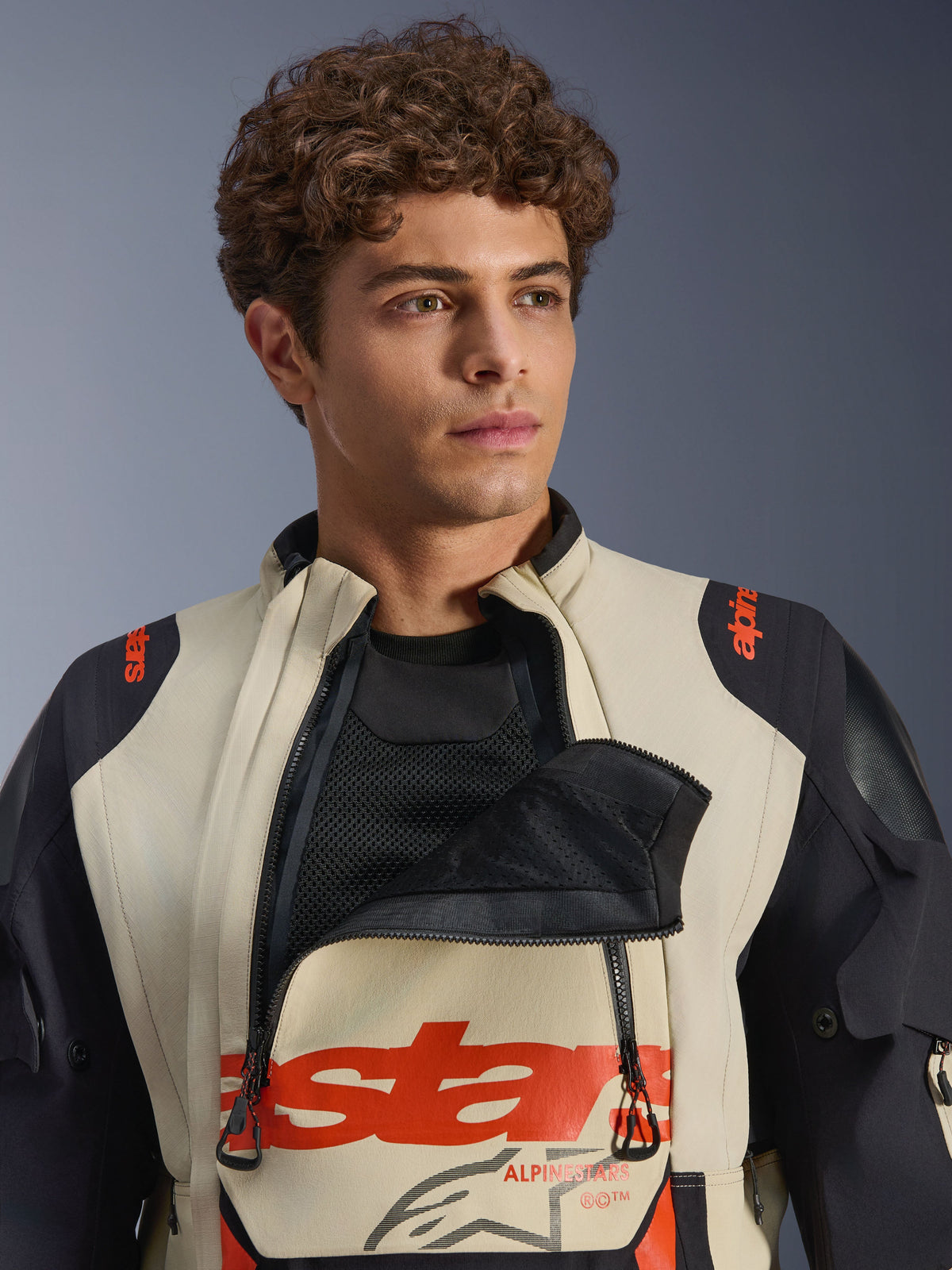 Alpinestars Halo Pro Drystar® XF laminierte Jacke in Mastic Black, männliches Model trägt die Jacke mit geöffnetem Brust-Belüftungspanel, um die Mesh-Unterschicht zu zeigen, mit rotem Branding und schwarzen Schulterpartien, technische Adventure-Motorradausrüstung
