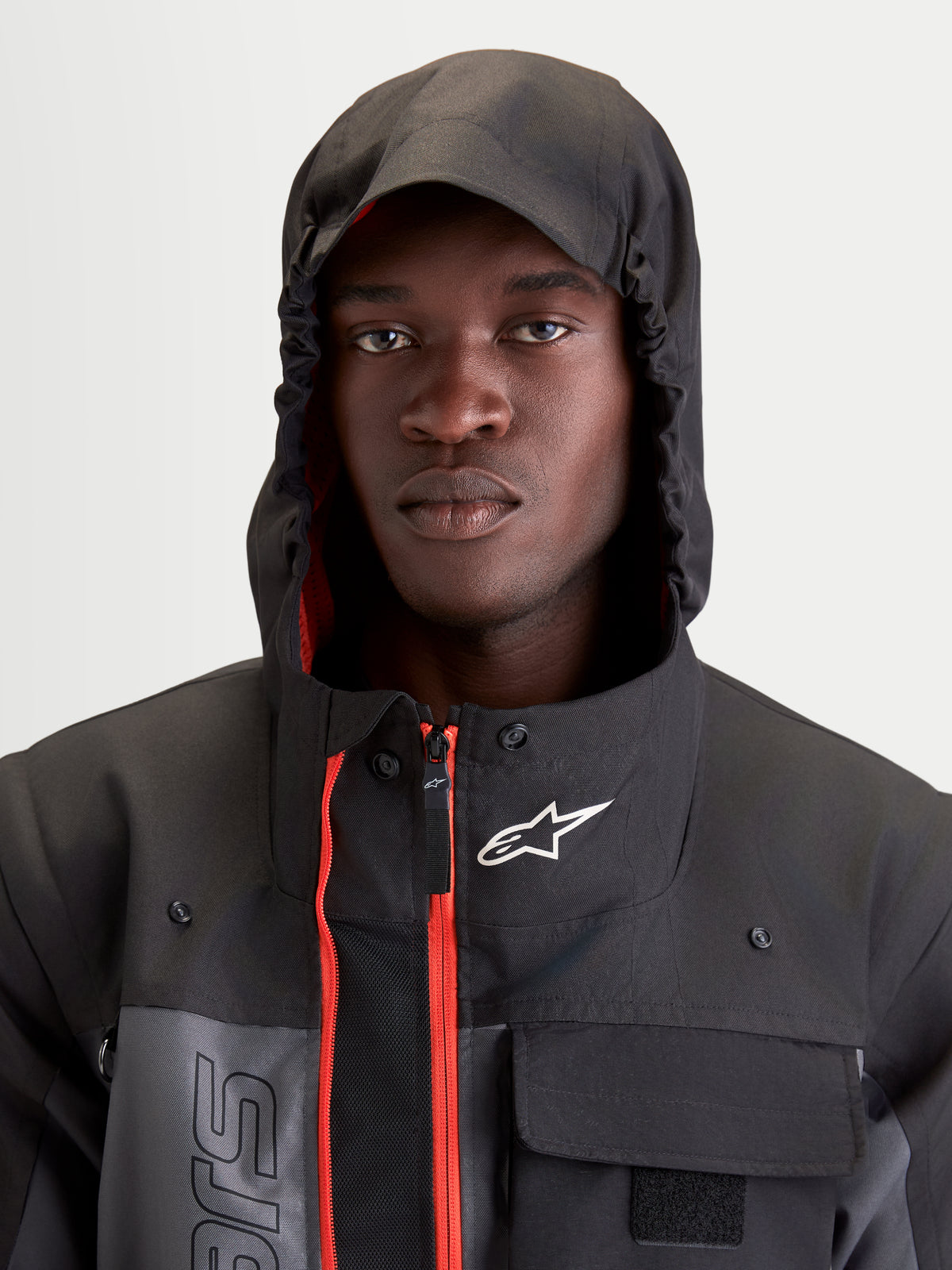 Alpinestars Morfex Parka Wp Jacke, urbane Herren-Motorradjacke in Mondgrau und Schwarz, Nahaufnahme eines Models mit hochgezogener Kapuze und sichtbaren roten Akzenten im Innenbereich