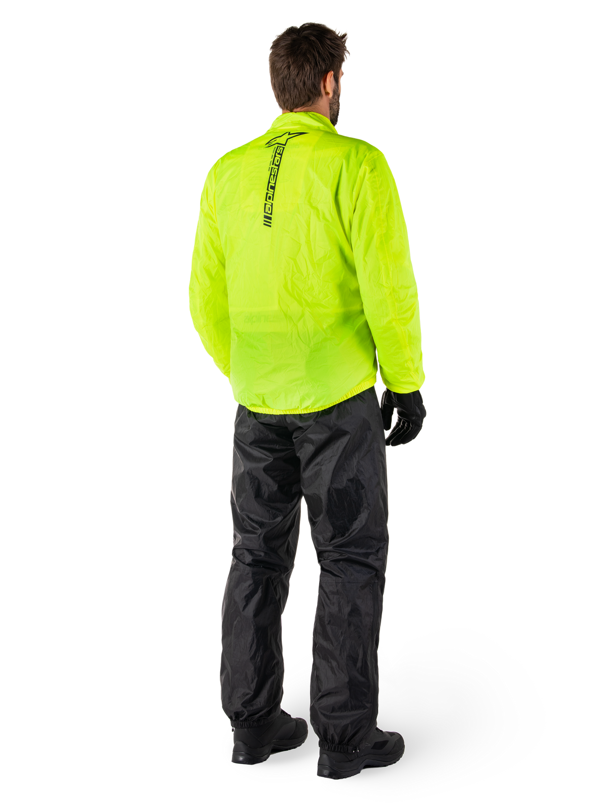 Person von hinten in Alpinestars Hurricane Rain V2 Jacke in Gelb Fluo und Hurricane Rain V2 Hose in Schwarz, vertikales Logo auf dem Jackenrücken, wasserdichte Motorrad-Regenbekleidung mit schwarzen Handschuhen und Stiefeln