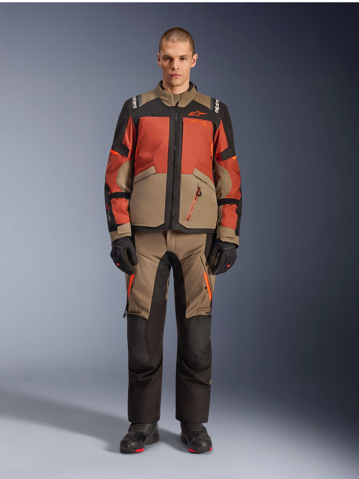Alpinestars Andes V4 Drystar® Jacke, Adventure-Motorradjacke, Walnut Rust Black, getragen mit passender Hose und Handschuhen, mehrfarbiges Design mit rostorangefarbenen und walnussbraunen Einsätzen, strapazierfähige Textilausrüstung für jedes Gelände