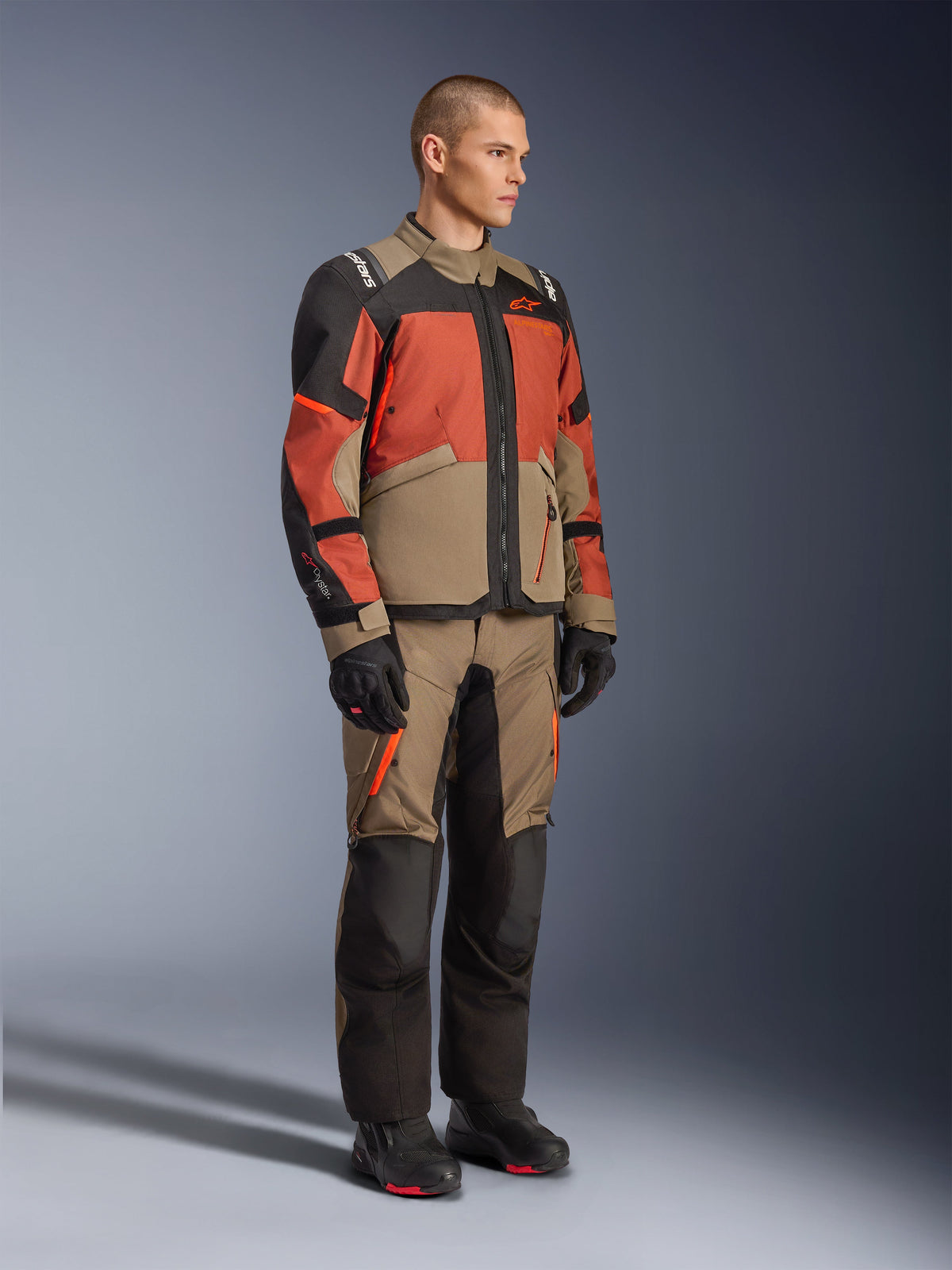 Alpinestars Andes V4 Drystar® Jacke, Adventure-Tourenjacke, Walnut Rust Black, getragen mit passender Hose und schwarzen Stiefeln, Color-Blocking-Design in Hellbraun, Rostrot und Schwarz, strapazierfähige Textilkonstruktion mit sichtbaren Reißverschlüssen und Alpinestars-Logos.