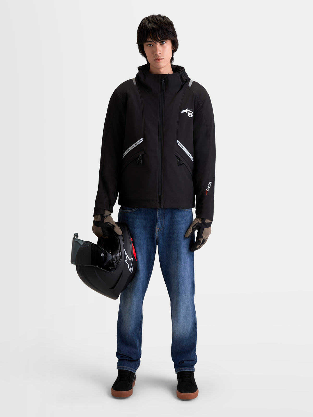 Alpinestars C 5 Drystar Jacke, urbane Motorrad-Textiljacke für Herren in Schwarz, Vorderansicht an einem Model mit Jeans und Handschuhen, die einen Helm halten, zeigt die wasserdichte Softshell-Konstruktion und die integrierte Kapuze