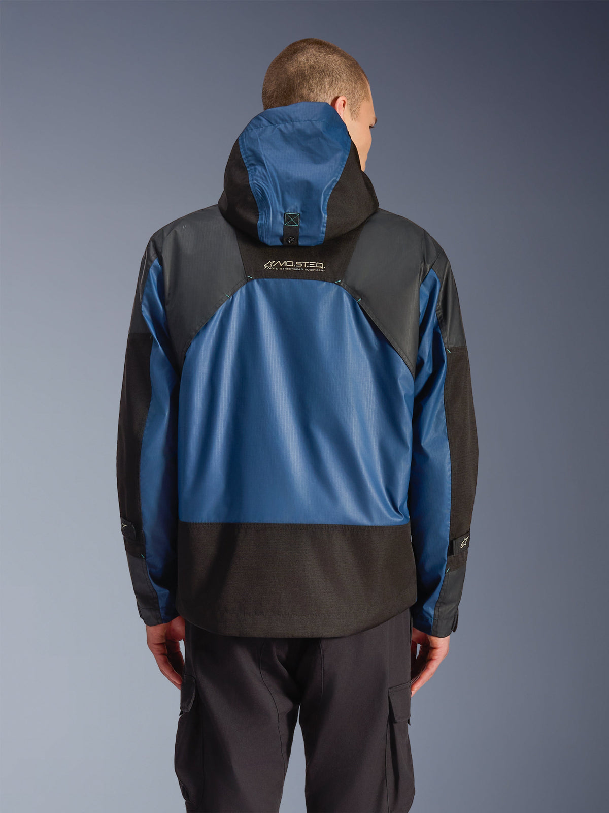 Alpinestars Mospher Waterproof Jacke in Black Dark Petrol, Rückansicht eines Motorrad-Parkas mit blauen Ripstop-Einsätzen und schwarzen verstärkten Bereichen, MO.ST.EQ. Branding auf dem oberen Rücken, modernes urban-taktisches Design