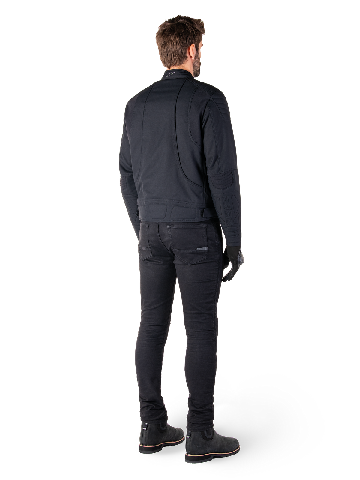 Rückansicht eines Fahrers in der schwarzen Alpinestars Clayton WR Jacke, mit gesteppten Paneelen an Ellbogen und Schultern, ergonomisch geschwungenen Nähten und reflektierenden Details am Kragen, kombiniert mit schwarzer Motorradhose und Stiefeln für einen urbanen Look.