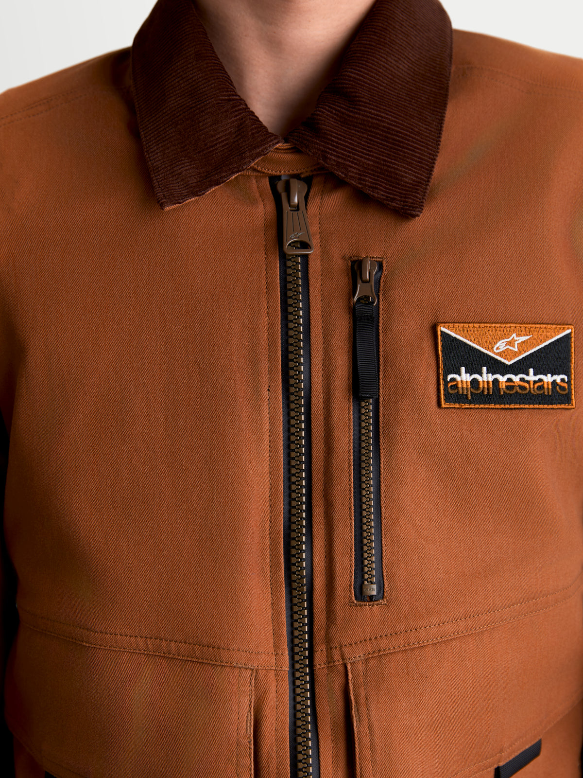 Alpinestars Mustang Wp Jacke, urbane Herren-Motorradjacke, Rostbraun und Dunkelbraun, Nahaufnahme der robusten Stretch-Twill-Konstruktion im Workwear-Stil mit Cordkragen, Frontreißverschluss und Brust-Logopatch