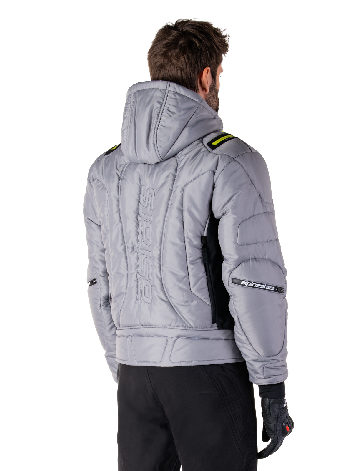 Alpinestars Mohobbs Waterproof Jacket in Lunar Gray and Lime Punch, rear view on a model, quilted padded bomber design with vertical embossed astars branding on the back, lime green shoulder accents, hooded, worn with black motorcycle pants and gloves.