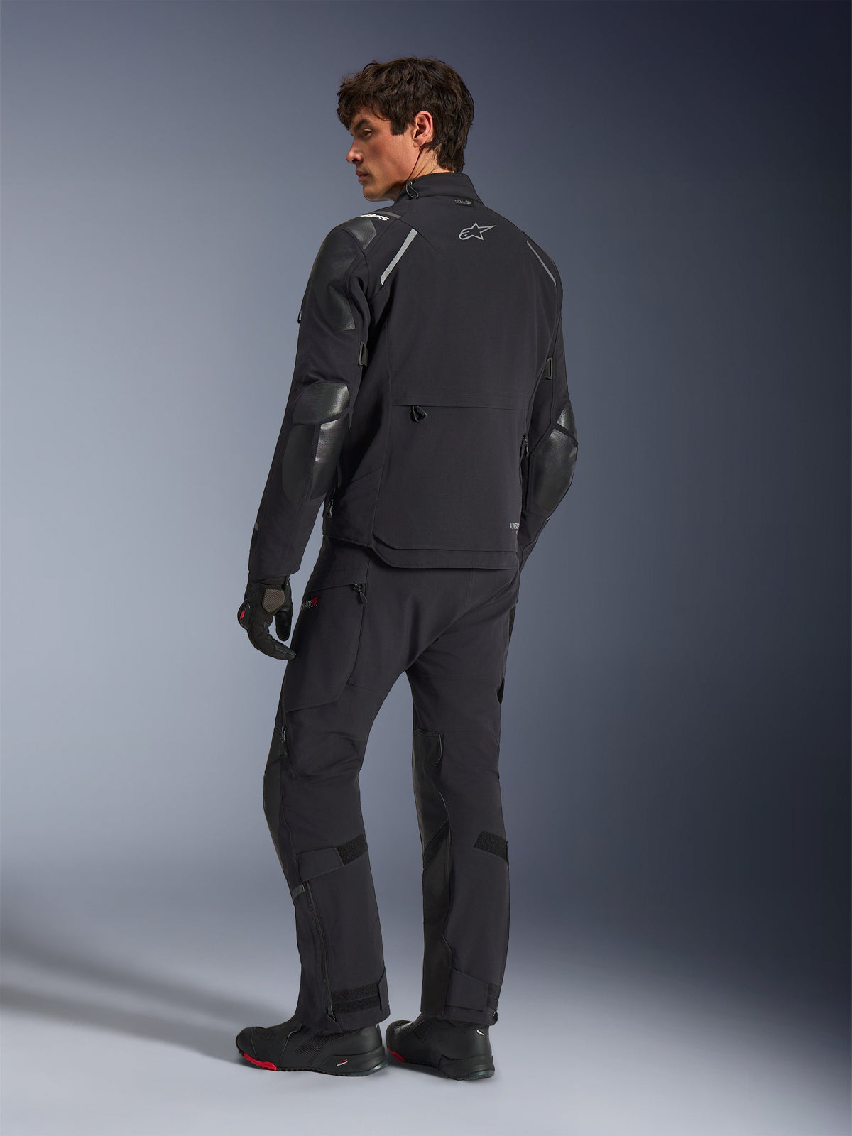 Alpinestars Andes Pro Drystar® XF Jacke, Adventure-Motorradjacke, Schwarz, Rückansicht getragen mit passender Hose und Stiefeln, mit verstärkten Einsätzen und silbernem Stern-Logo, technische Allwetter-Fahrausrüstung