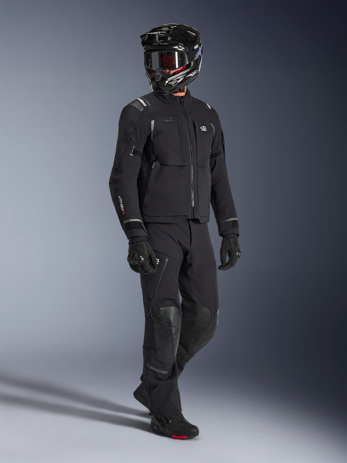 Alpinestars Andes Pro Drystar® XF Jacke, Adventure-Motorradjacke in Schwarz und Dunkelgrau, getragen mit passender schwarzer Textilhose, schwarzem Integralhelm mit Brille, Handschuhen und Stiefeln, mit einer laminierten 3-Lagen-Schale und mehreren Taschen für Ganzjahres-Abenteuerfahrten.