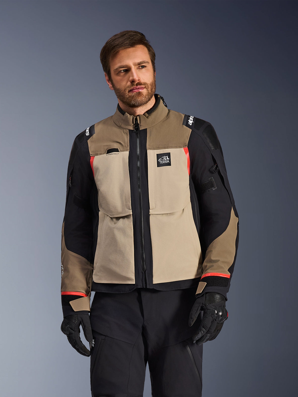 Alpinestars Andes Pro Drystar® XF Jacket, Walnut Aluminum, motorcycle adventure jacket featuring tan and black panels with red accents, worn with black riding pants and gloves, technical waterproof touring gear