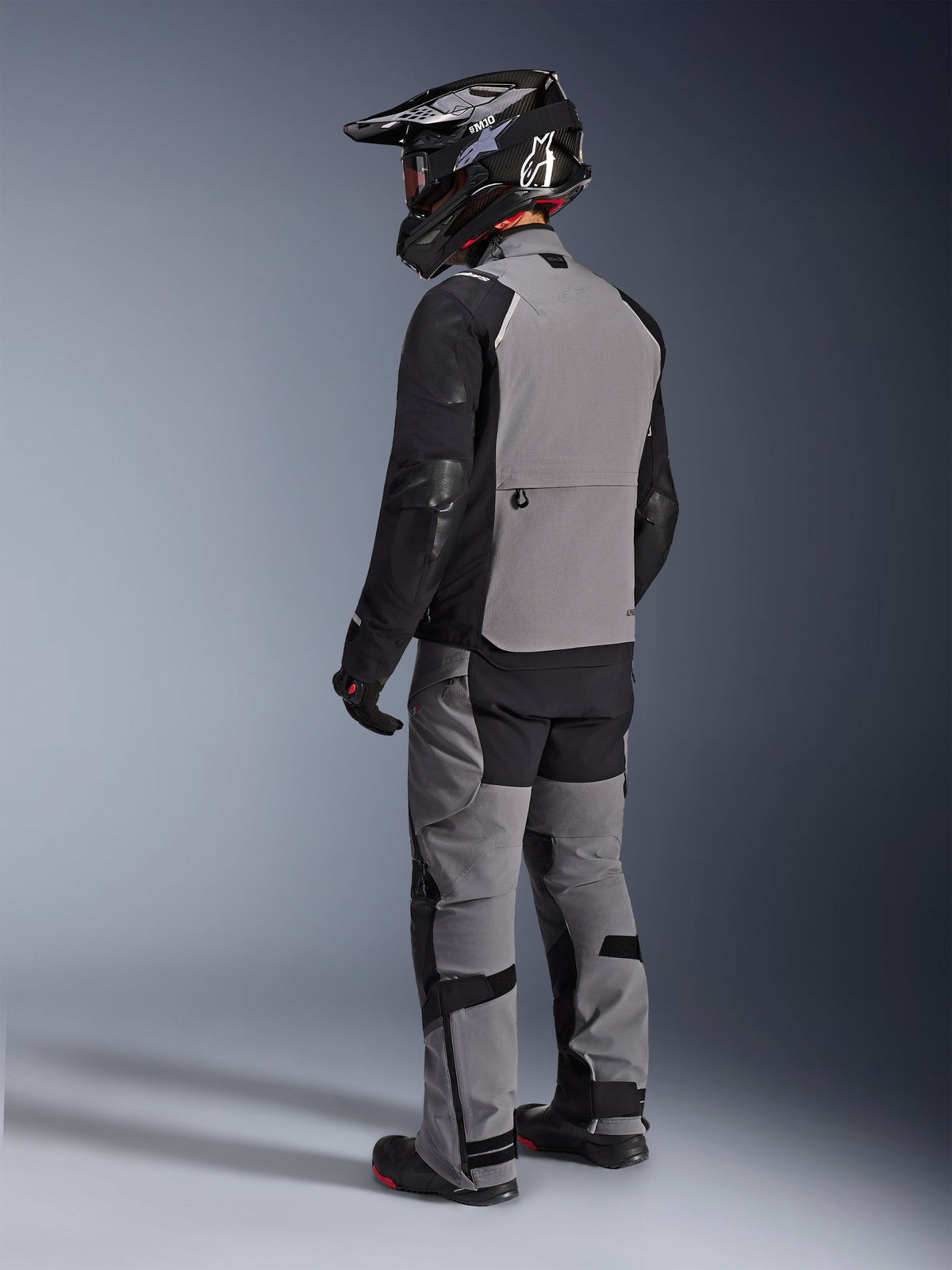Alpinestars Andes Pro Drystar® XF Jacke, Adventure-Motorradjacke, Dunkelgrau und Schwarz, Rückansicht mit grauem Rückenteil und schwarzen Ärmeln, getragen mit passender Hose und schwarzem Helm, technische Allwetter-Fahrausrüstung