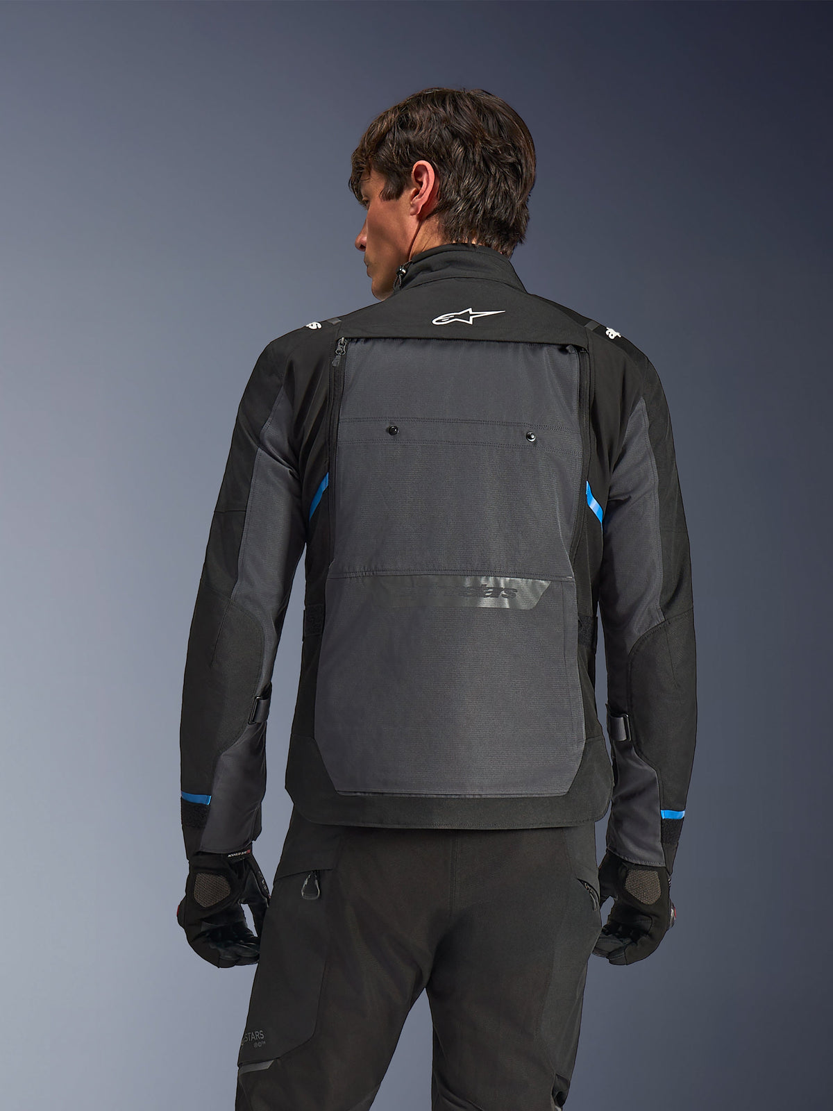 Alpinestars Cusco Drystar® Jacke, Motorradjacke, Schwarz und Dunkelgrau, Rückansicht an einem Model mit großem grauen Rückenteil, weißem Alpinestars-Logo und blauen Akzenten an den Ärmeln.