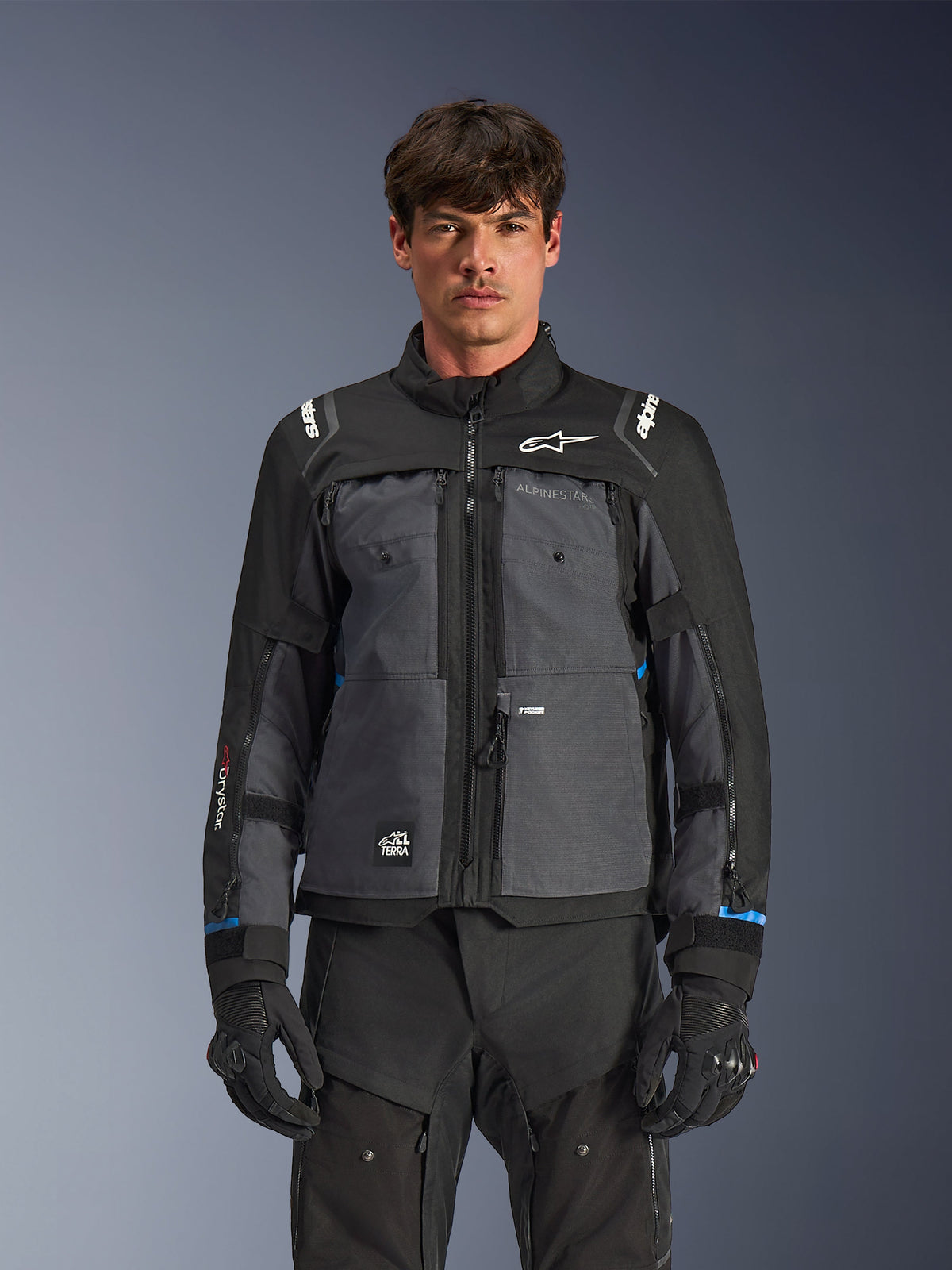 Alpinestars Cusco Drystar® Jacke, Motorrad-Tourenjacke, Schwarz und Dunkelgrau, Vorderansicht am Modell, mit Alpinestars-Logos auf Brust und Schultern, Drystar®-Branding am Ärmel, technisches Multi-Pocket-Design mit Belüftungsreißverschlüssen, kombiniert mit schwarzer Motorradausrüstung