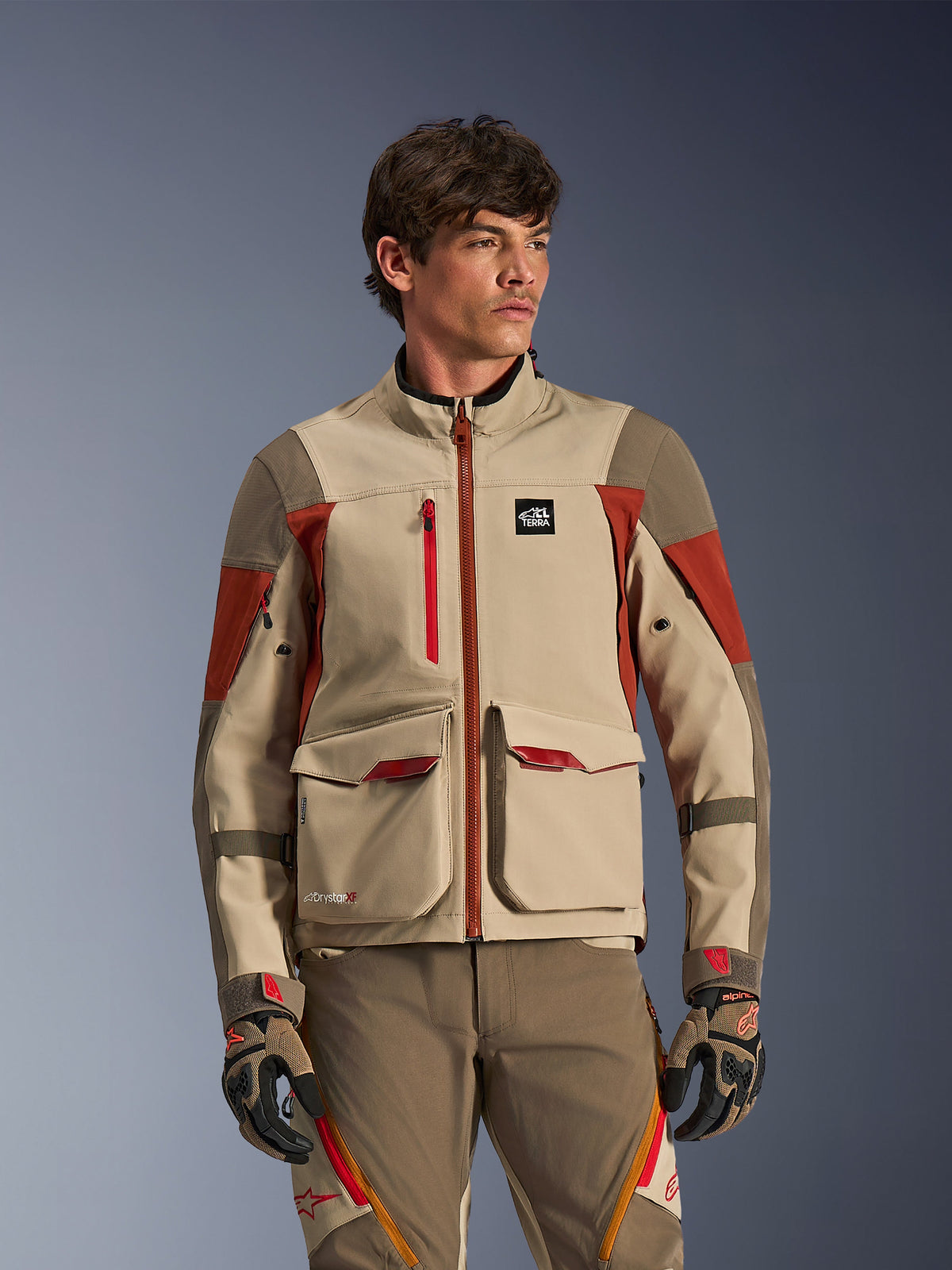 Alpinestars Maxdura Drystar®XF Laminated Armored Shell, Aluminum Walnut Rust Brown, Adventure motorcycle jacket worn by a male model, featuring large front cargo pockets and technical red accents, paired with matching adventure riding pants and gloves