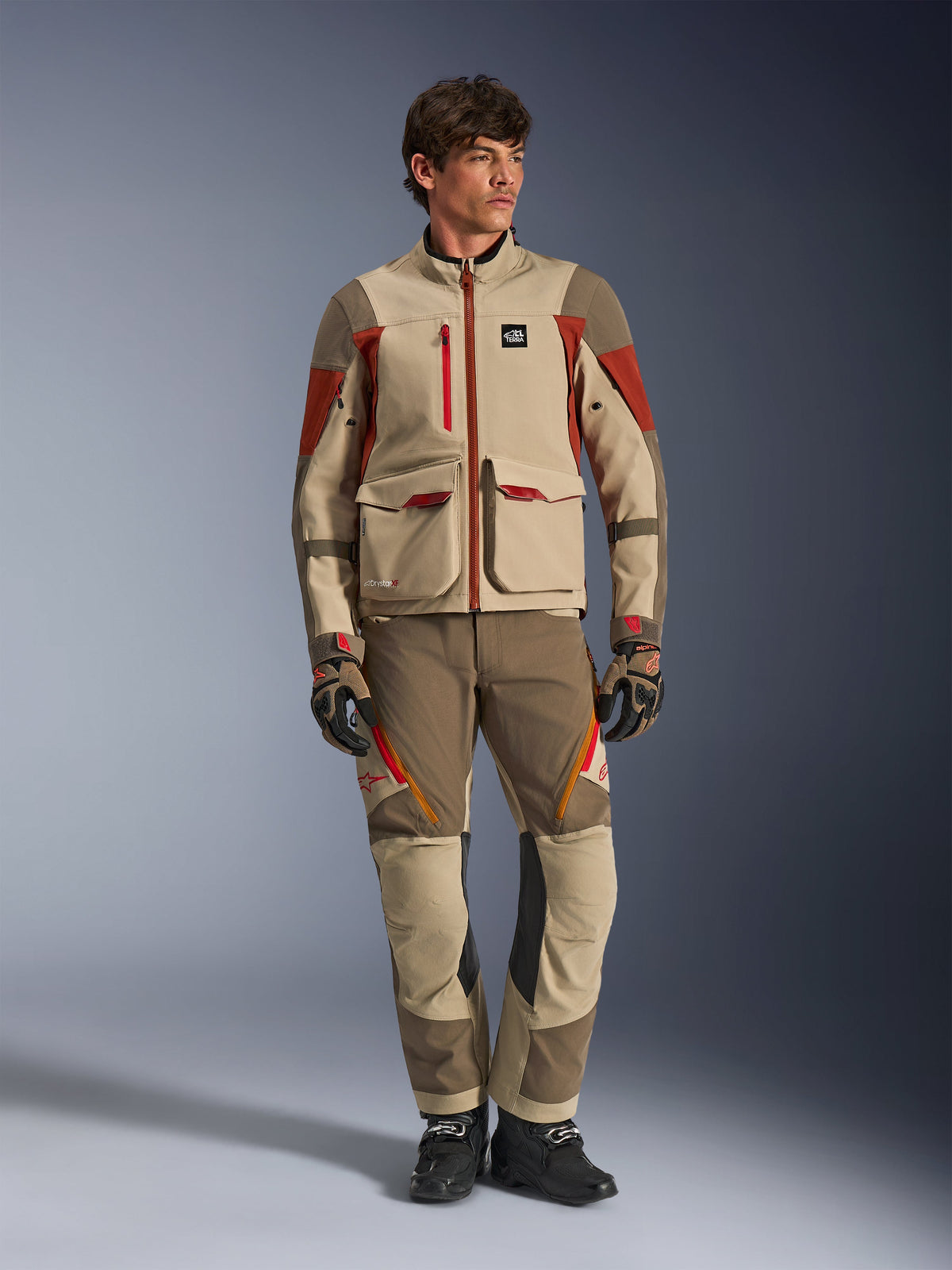 Maxdura Drystar®XF Laminated Armored Shell, adventure motorcycle jacket in Aluminum Walnut Rust Brown, worn by a male model with matching adventure pants, gloves, and boots, full-body studio shot of professional touring gear.