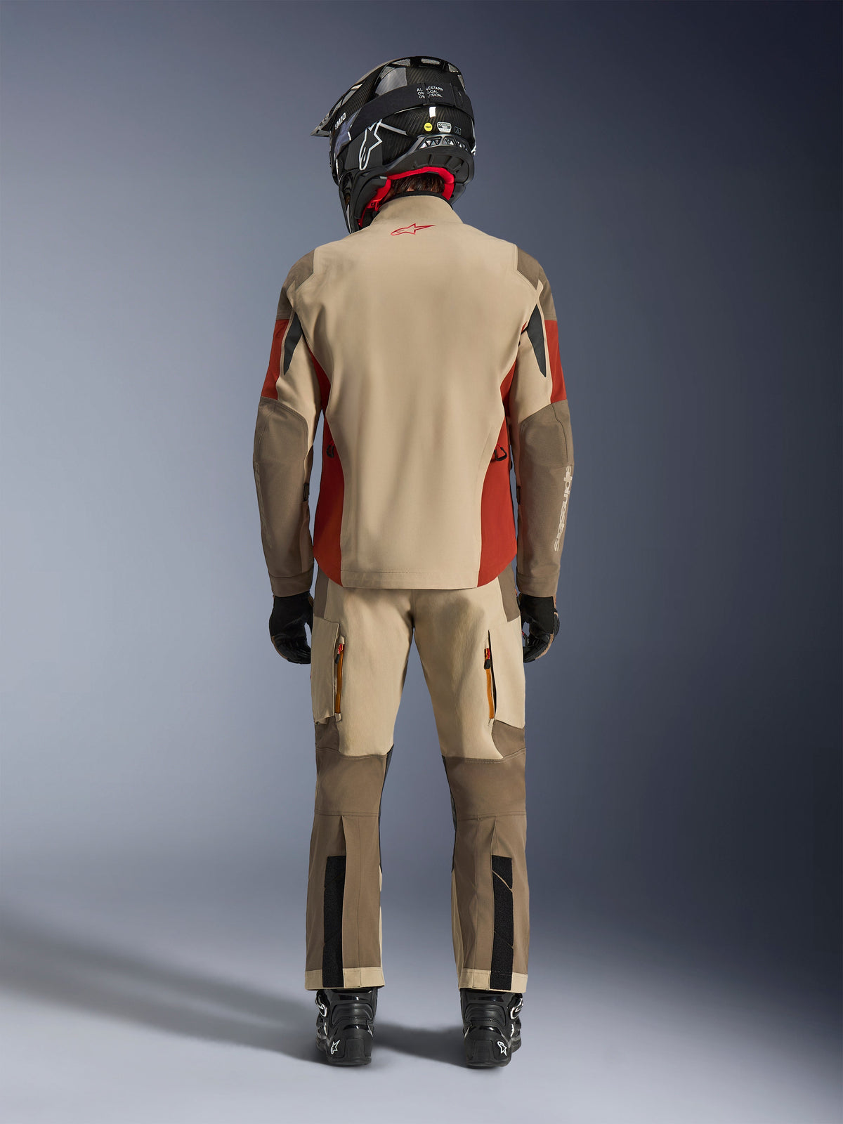 Alpinestars Maxdura Drystar®XF Laminated Armored Shell, adventure motorcycle jacket and matching pants, Aluminum Walnut and Rust Brown colorway, back view of rider with black helmet and boots, professional adventure-touring gear